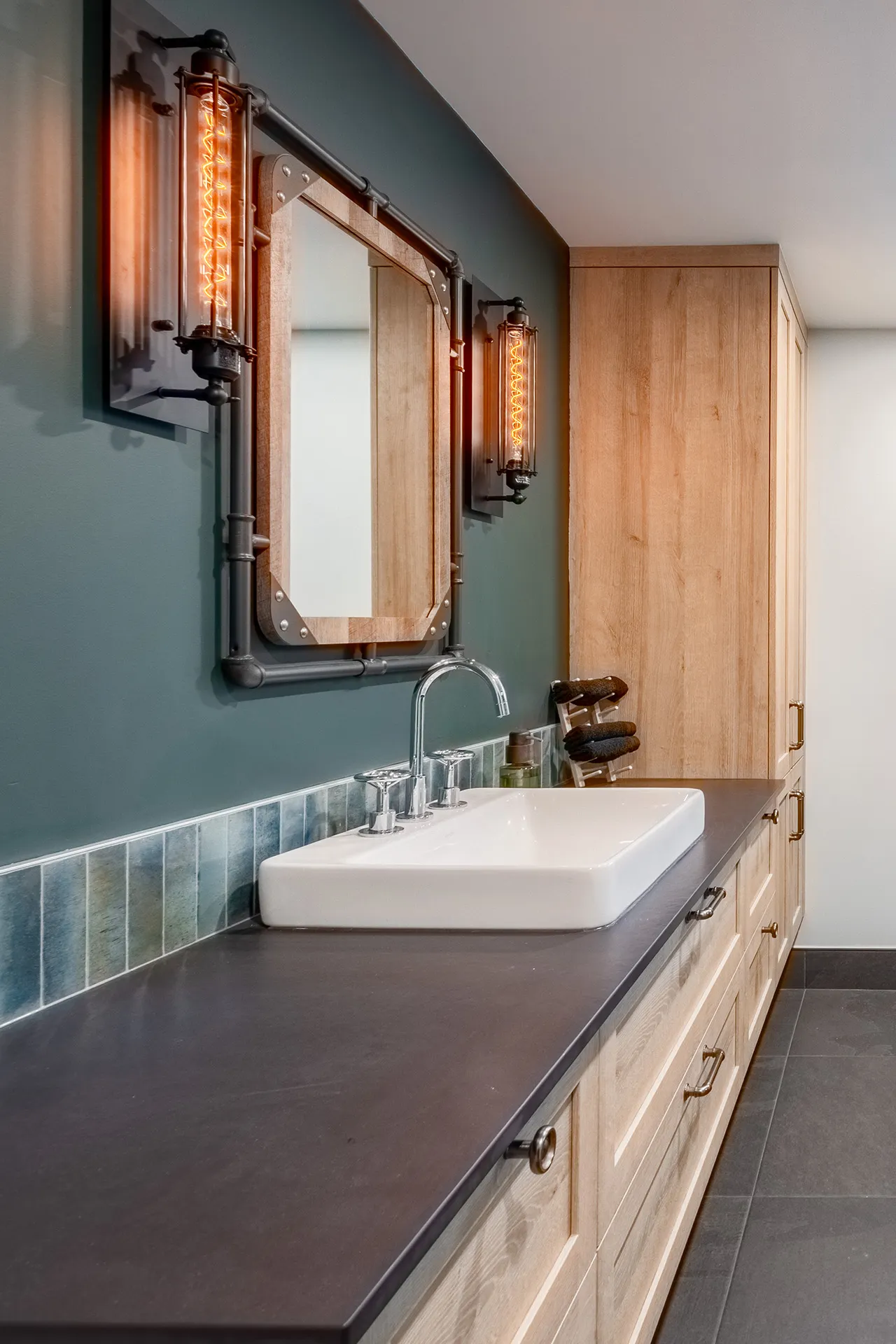 Lemay bathroom: light wood cabinets, dark grey countertop, white vessel sink, wood mirror, industrial lighting