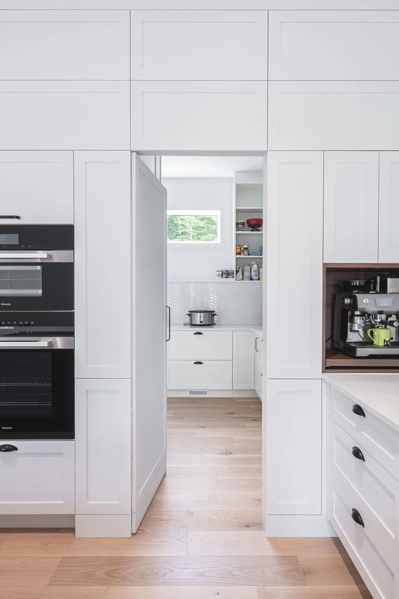 Modern all-white kitchen with custom Menuitech cabinetry, light countertop, subway tile backsplash, integrated black appliances