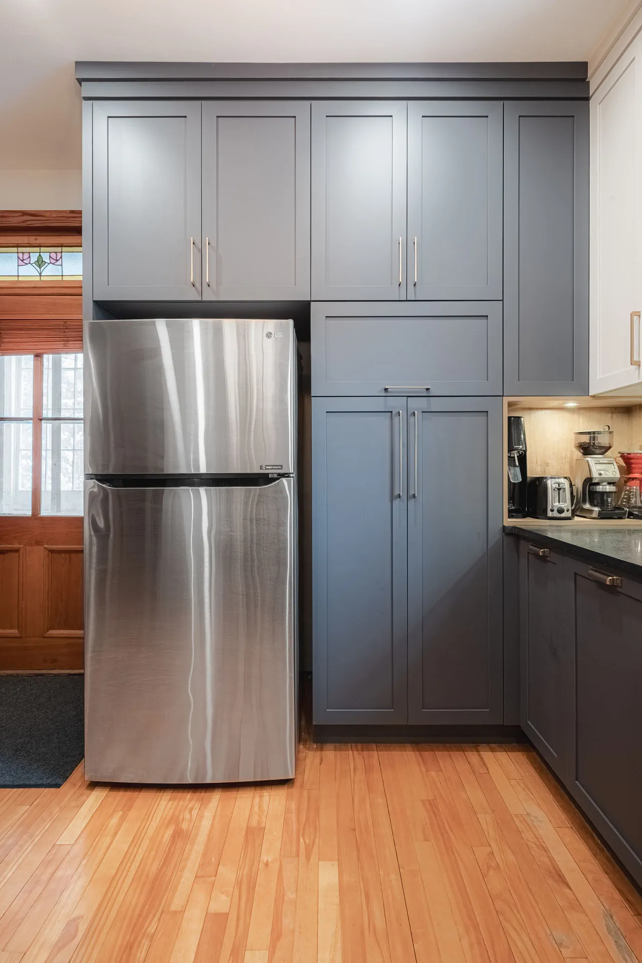Stephan kitchen: grey Menuitech cabinets, black countertop, stainless steel fridge, hardwood flooring, closed storage units