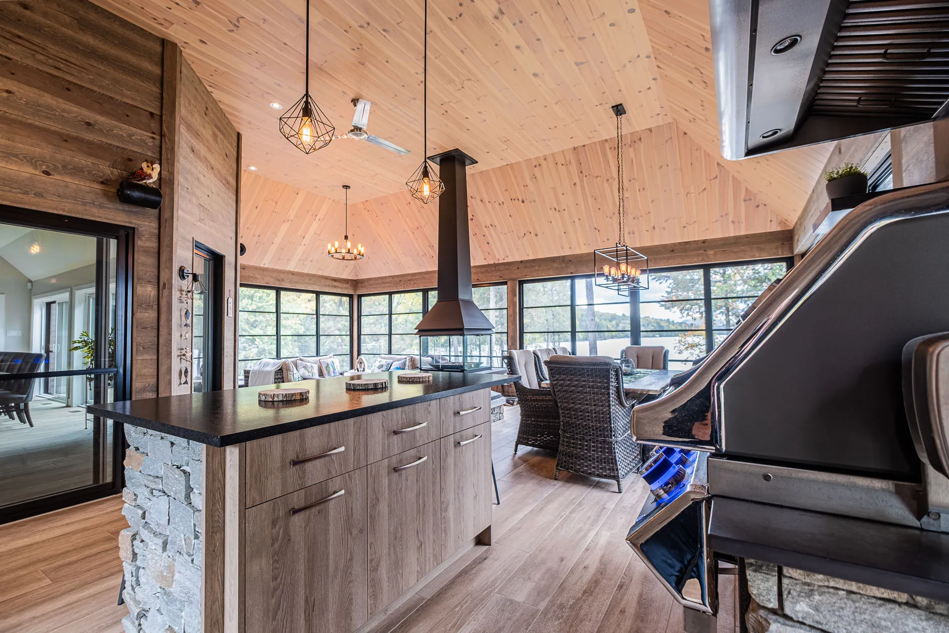 Modern kitchen with gray wood island, black countertop, stone backsplash, vaulted wood ceiling, geometric pendant lights