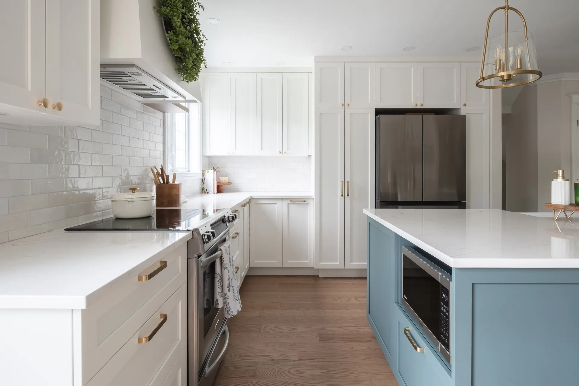 White and powder blue kitchen with white countertops, island, subway tile backsplash and brass pendant light
