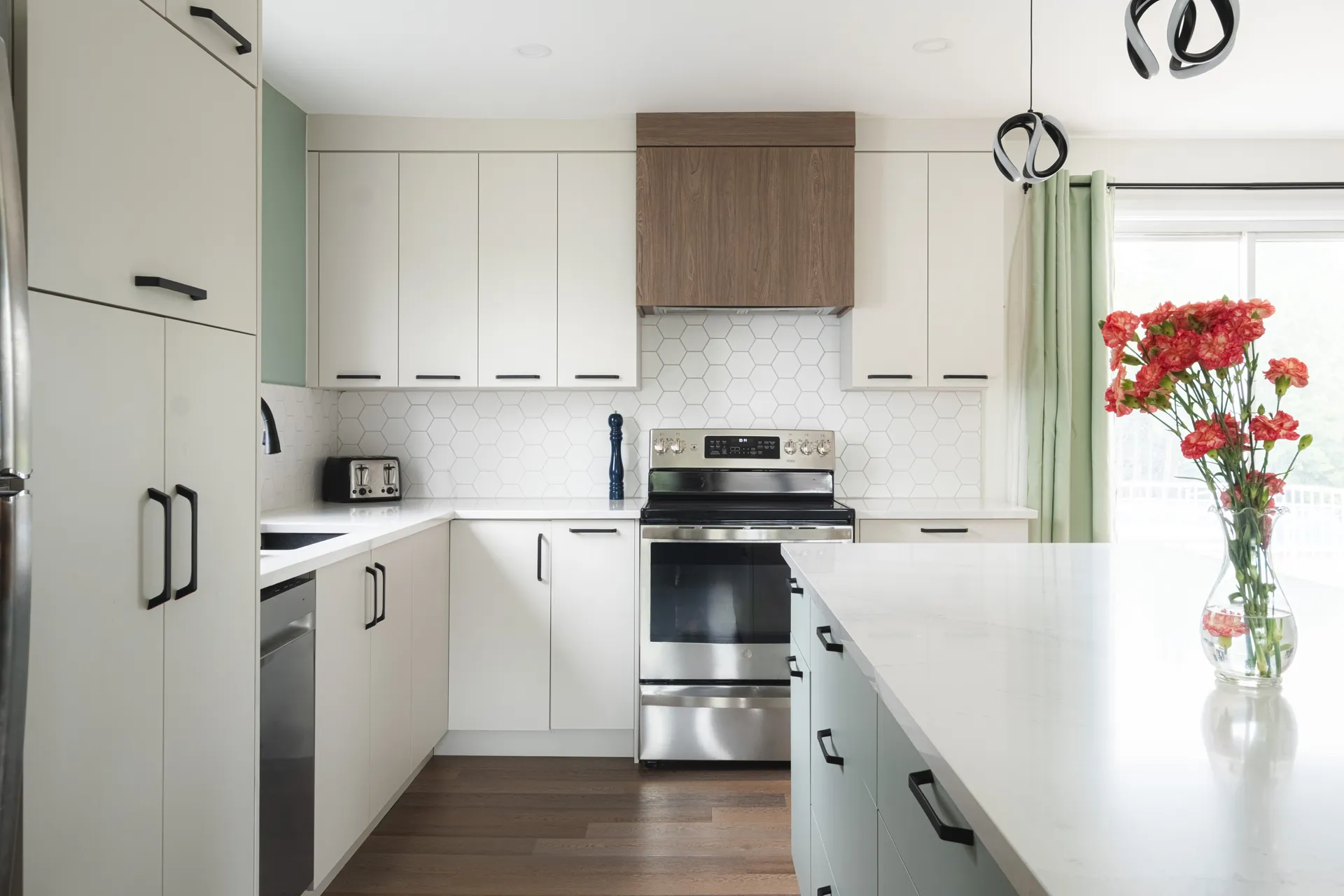 Modern white kitchen with custom Menuitech cabinetry, white countertop, hexagonal backsplash, island and stainless steel appliances