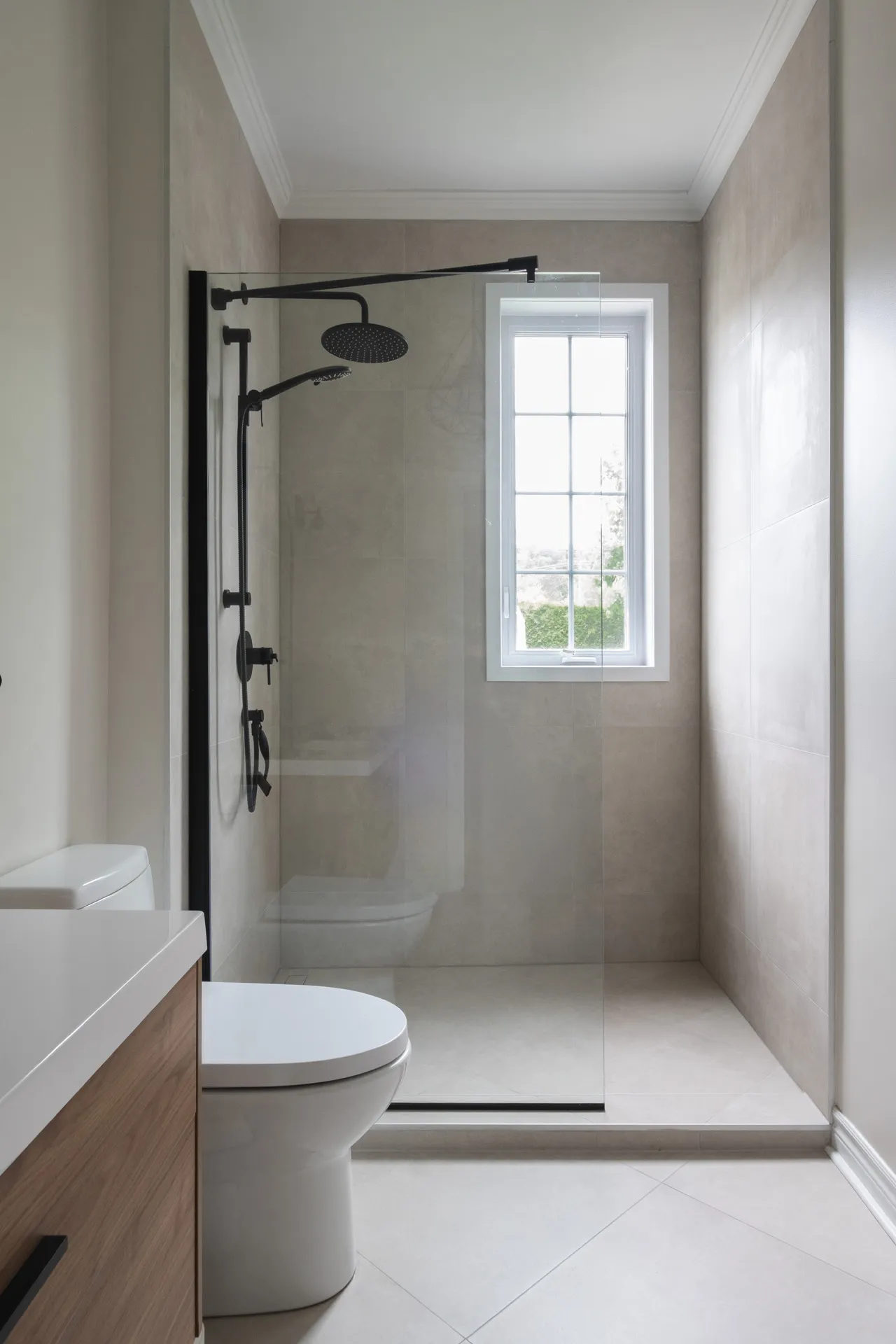 Modern bathroom with wood vanity, white toilet, black glass shower enclosure, dual showerheads and window