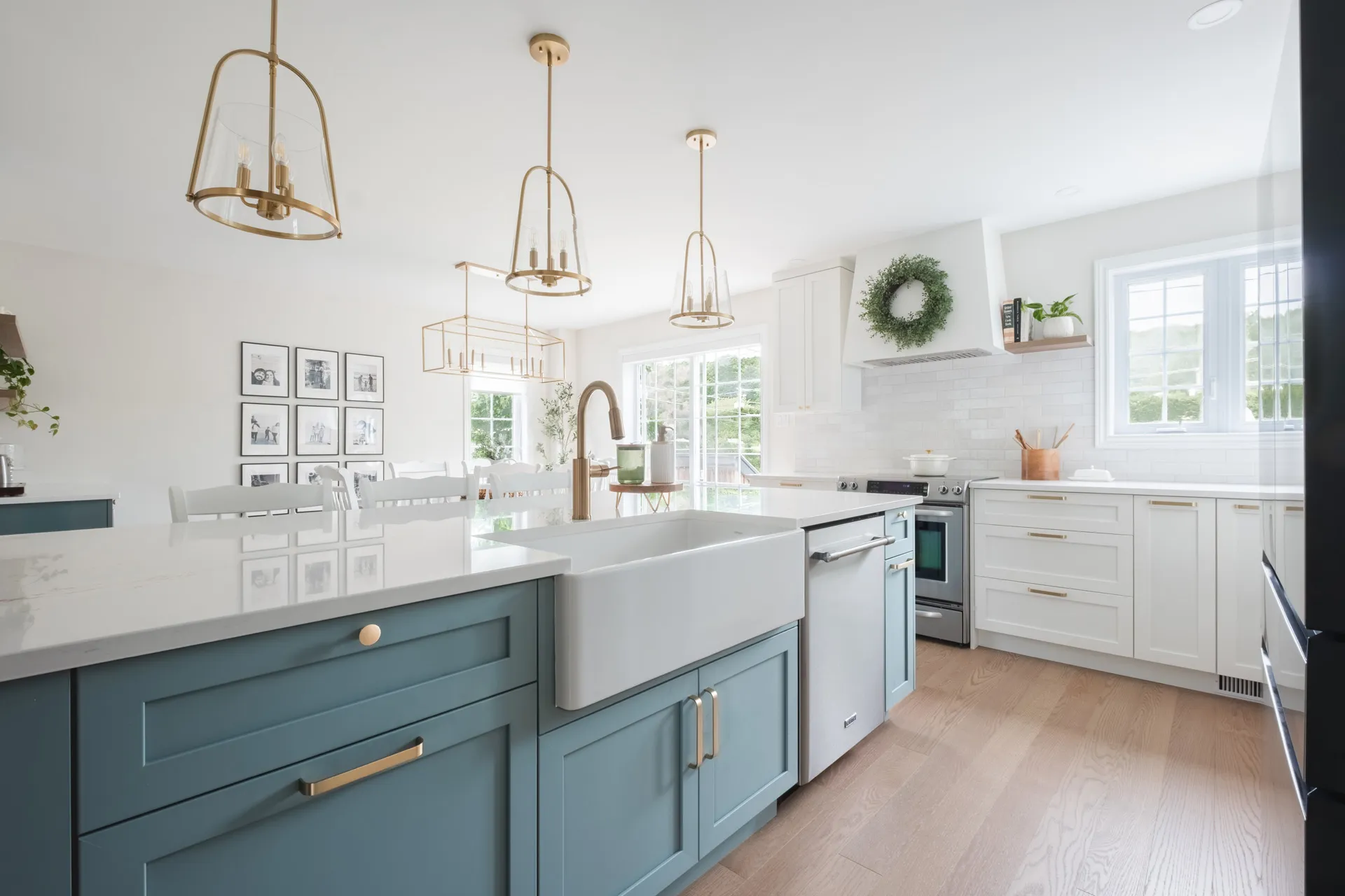 Modern Menuitech kitchen with teal and white cabinetry, grey countertop, island with farmhouse sink, white subway backsplash and brass pendant lights.