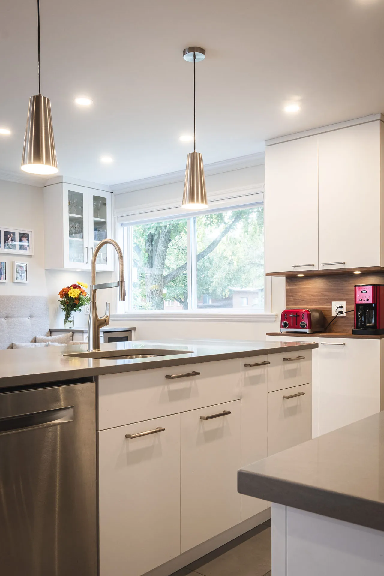 Modern Menuitech kitchen with white cabinets, dark grey countertops, central island, wood backsplash, brass pendant lights