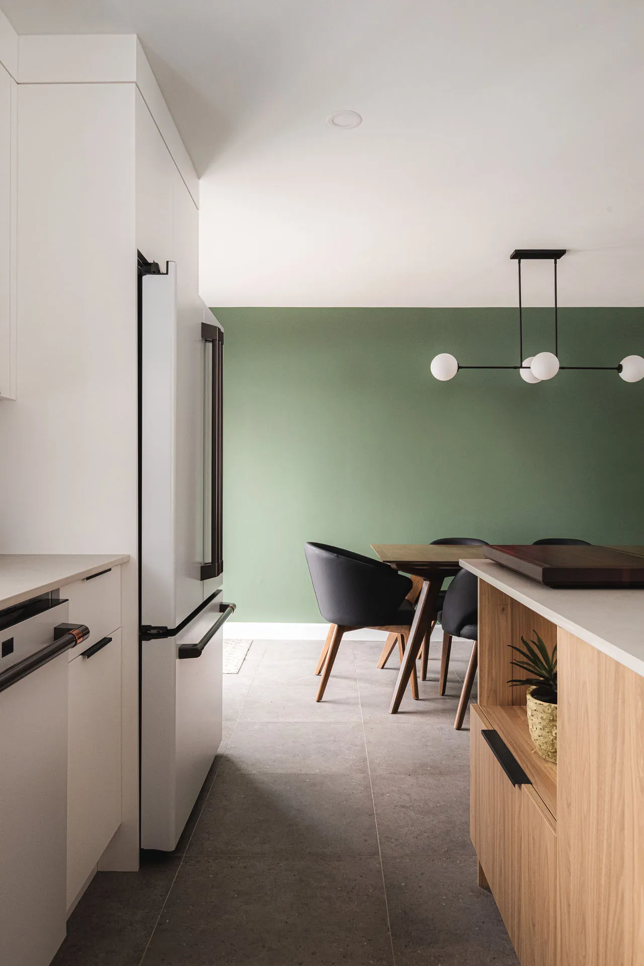 Modern Robitaille kitchen with white cabinets, white countertop, wooden island, sage green backsplash and globe pendant lights