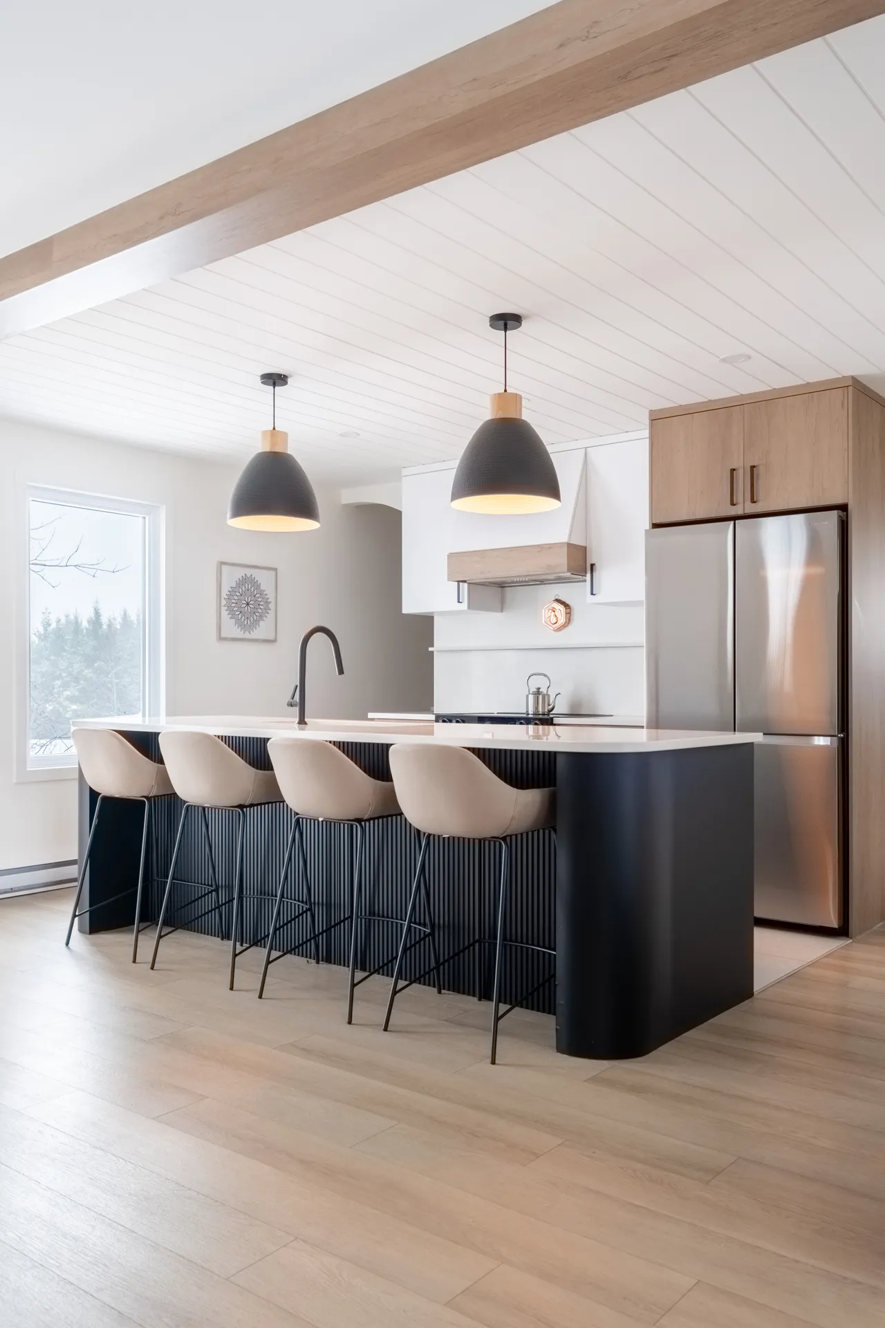 Cuisine moderne Alarie avec îlot noir, armoires blanches et bois, comptoir blanc, pendentifs noirs et poutres apparentes