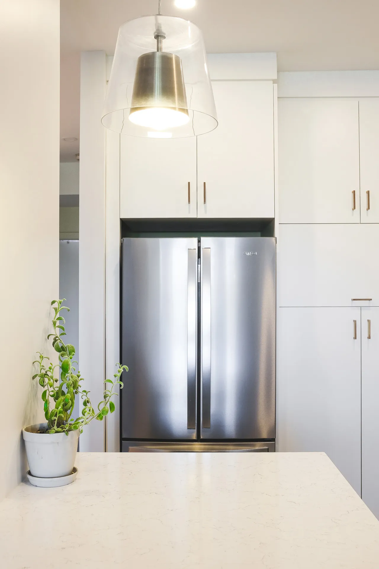 Modern Cavanagh kitchen with white cabinetry, marble countertop, stainless steel refrigerator and brass pendant lighting