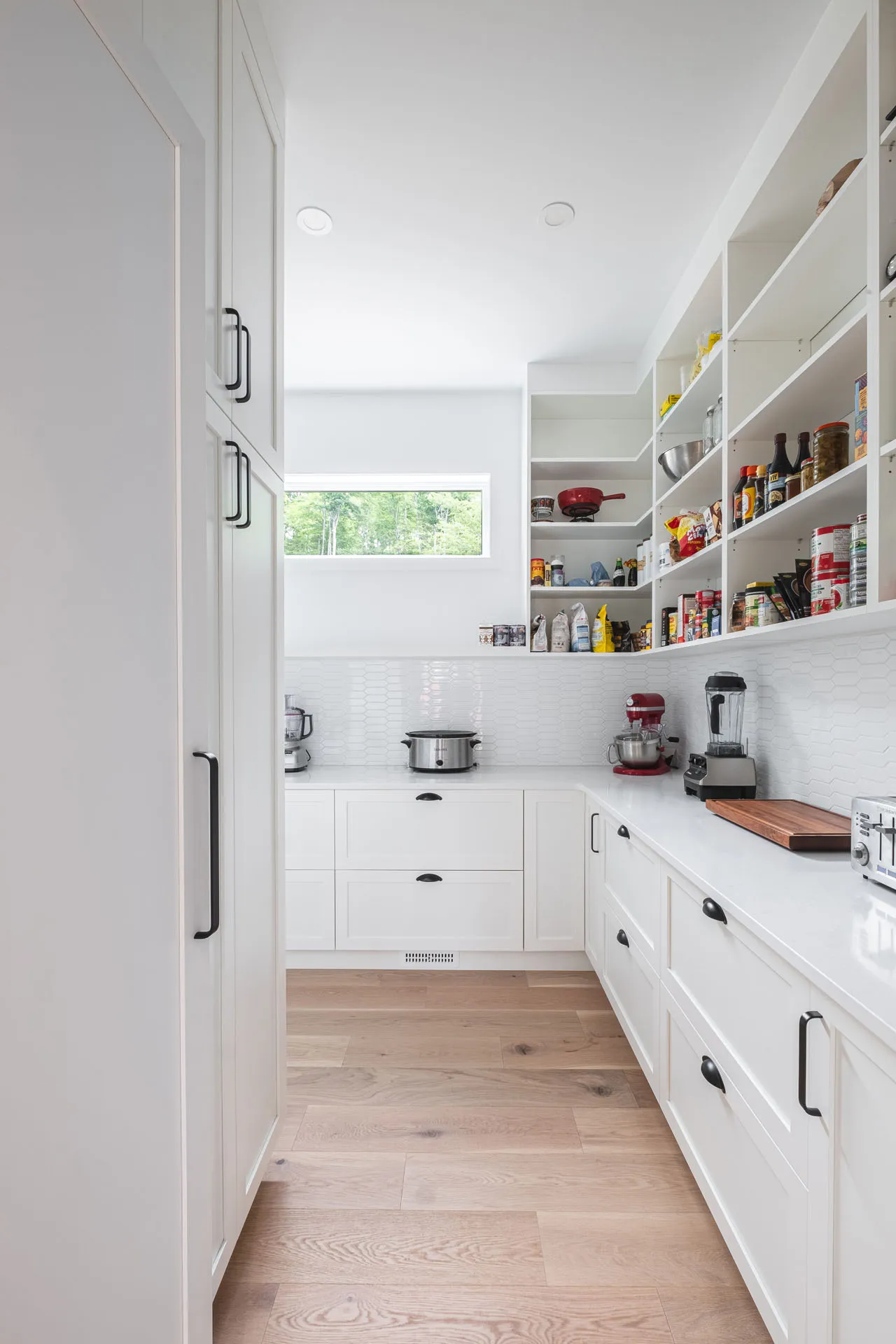 Modern white kitchen with custom cabinetry, white countertop, subway tile backsplash, island, open shelving and panoramic window