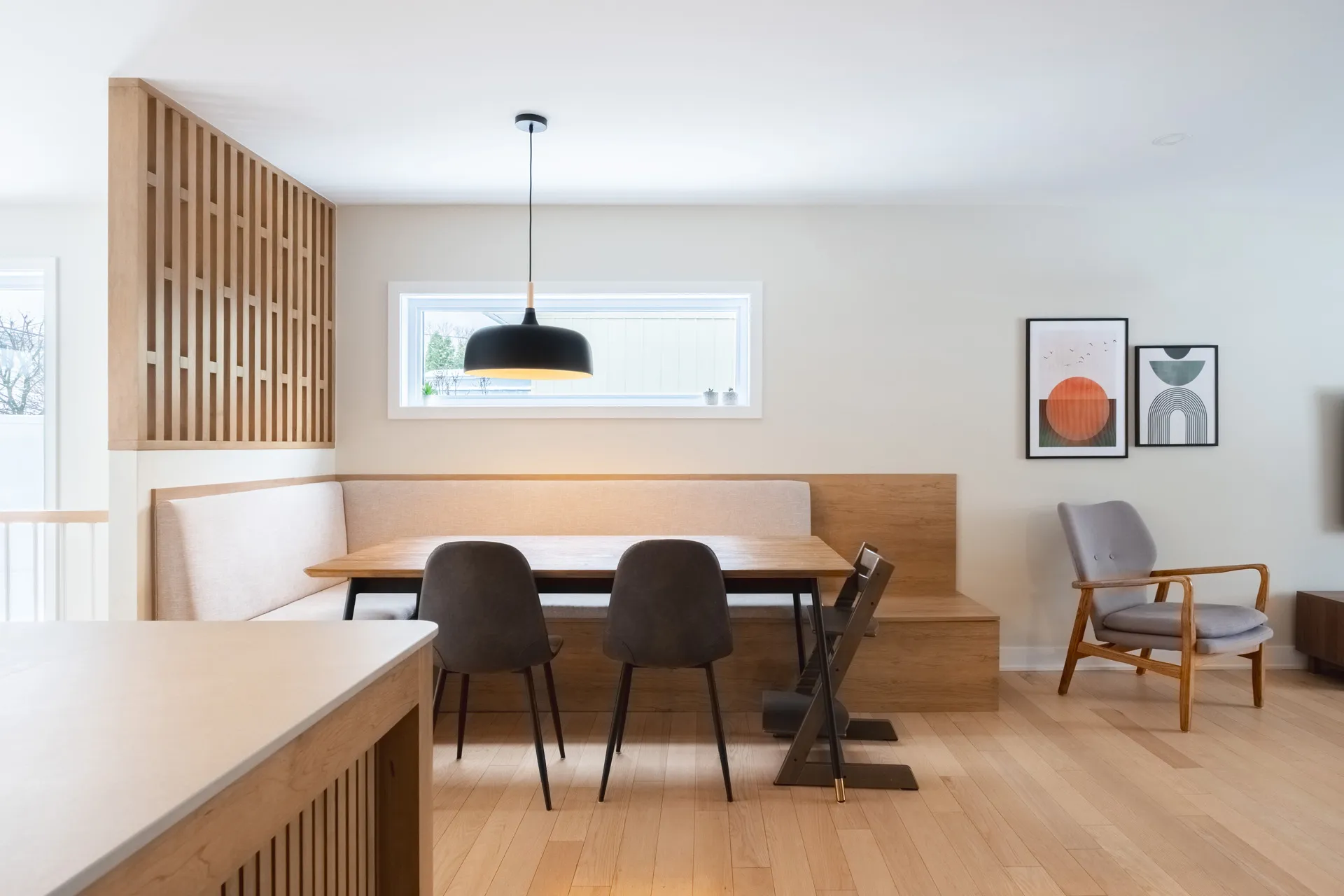Cuisine moderne Blainville : armoires chêne clair à lattes, comptoir blanc cassé, îlot bois, chaises noires, luminaire suspendu noir
