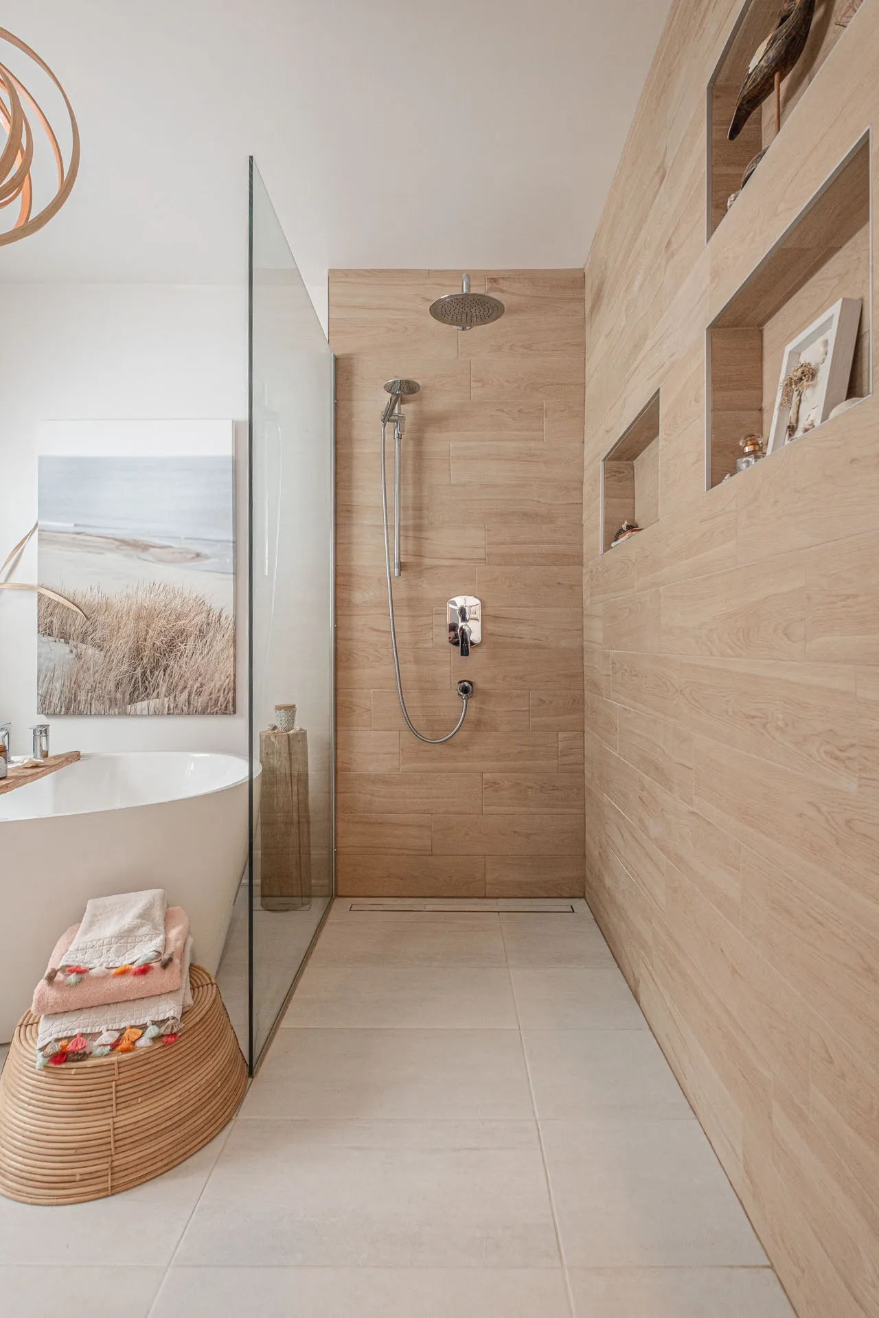 Modern bathroom with natural wood cabinets, white bathtub, wood-tiled shower and wall shelving niches