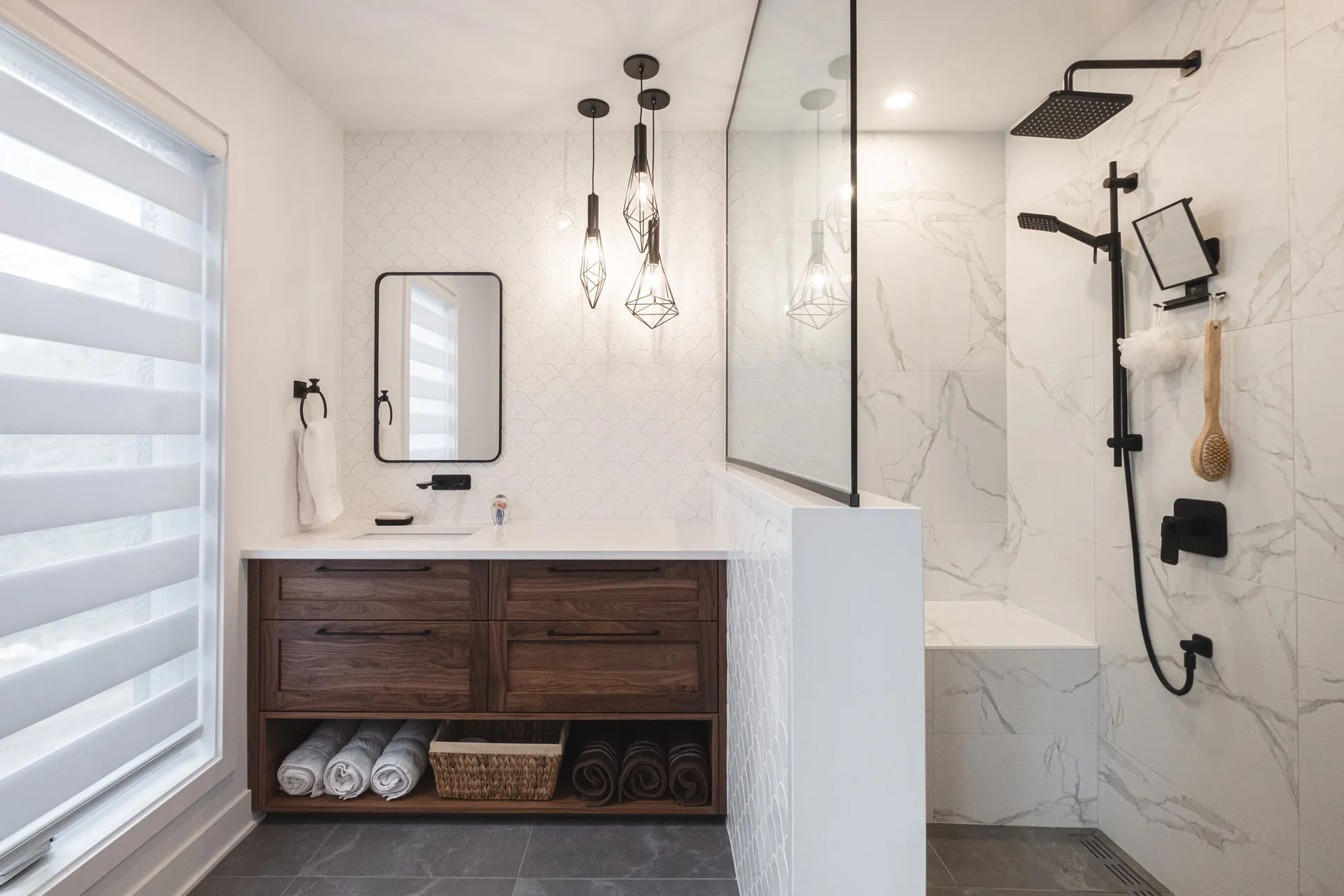 Menuitech bathroom with dark wood vanity, white countertop, marble backsplash, black mirror and geometric pendant lights