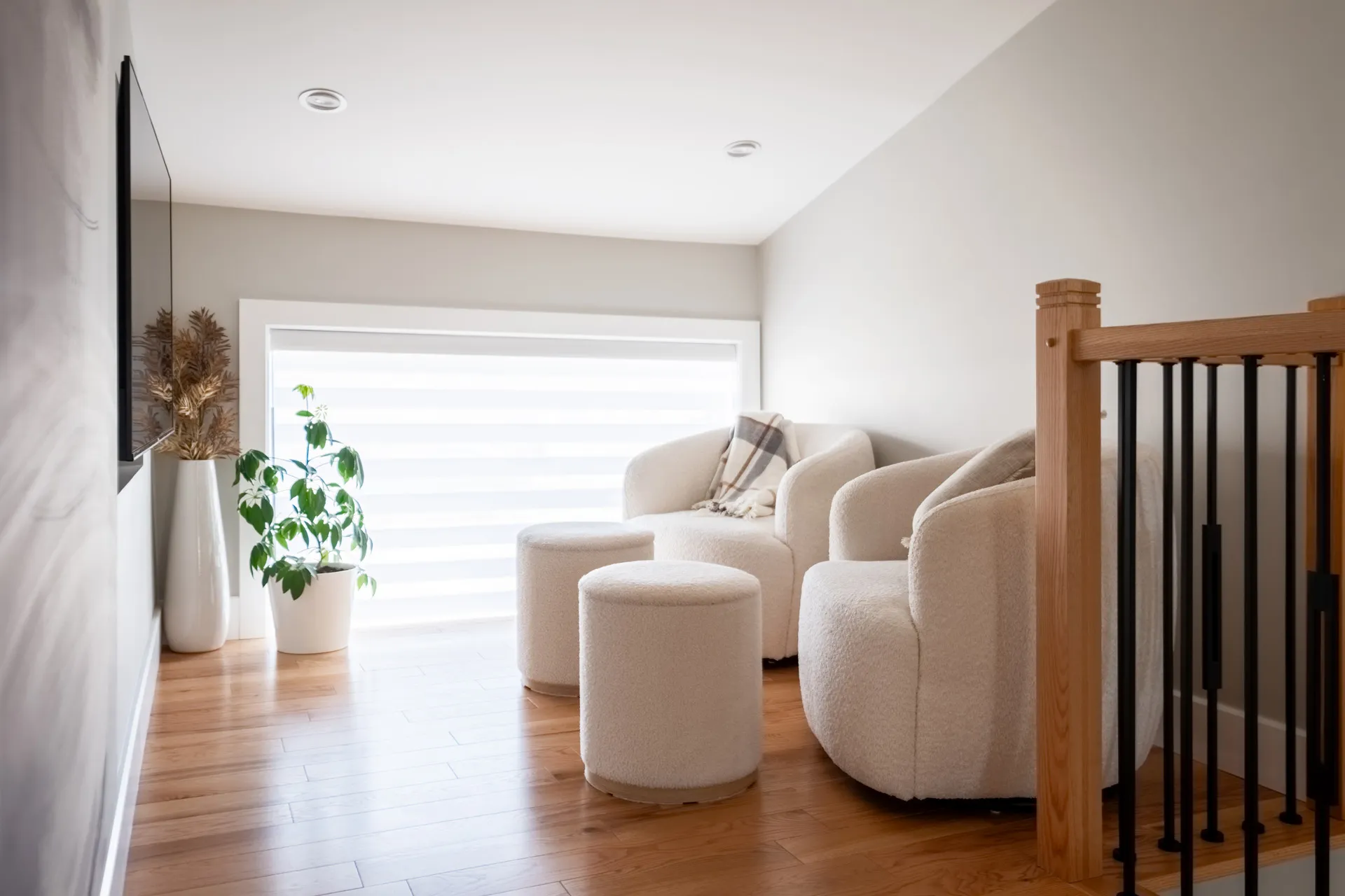 Loft moderne Laval: escalier bois, fauteuils crème bouclés, ottomans, baie vitrée, plantes vertes, plancher bois