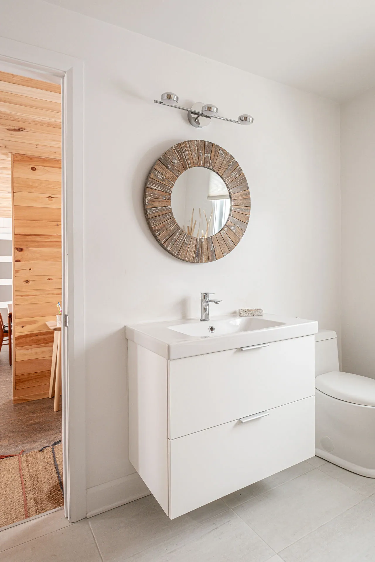 Modern bathroom with white two-drawer vanity, white countertop and natural wood round mirror