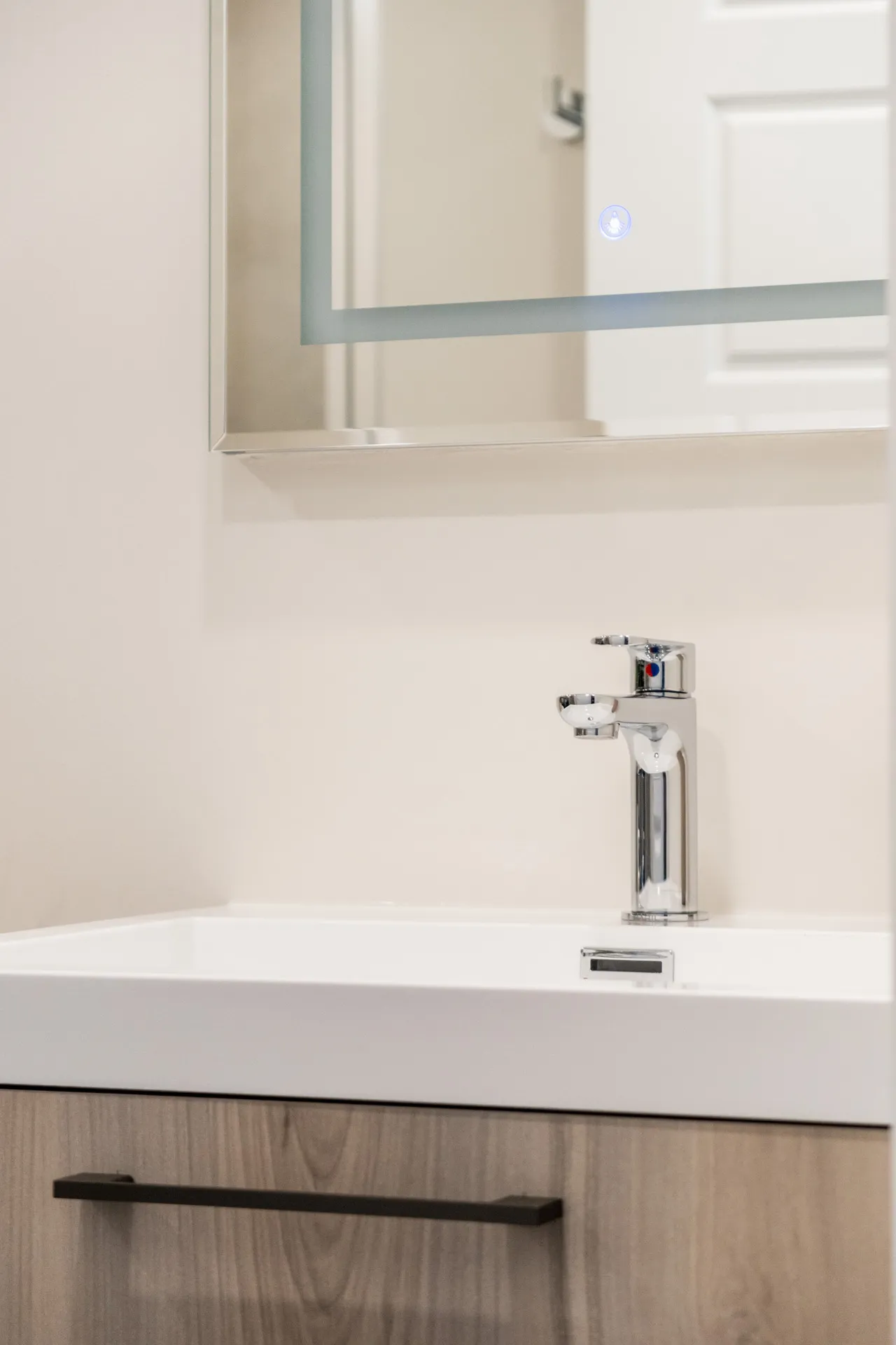 Salle de bain Forand : vanité bois clair, comptoir blanc, robinet chrome, miroir éclairé, dosseret beige