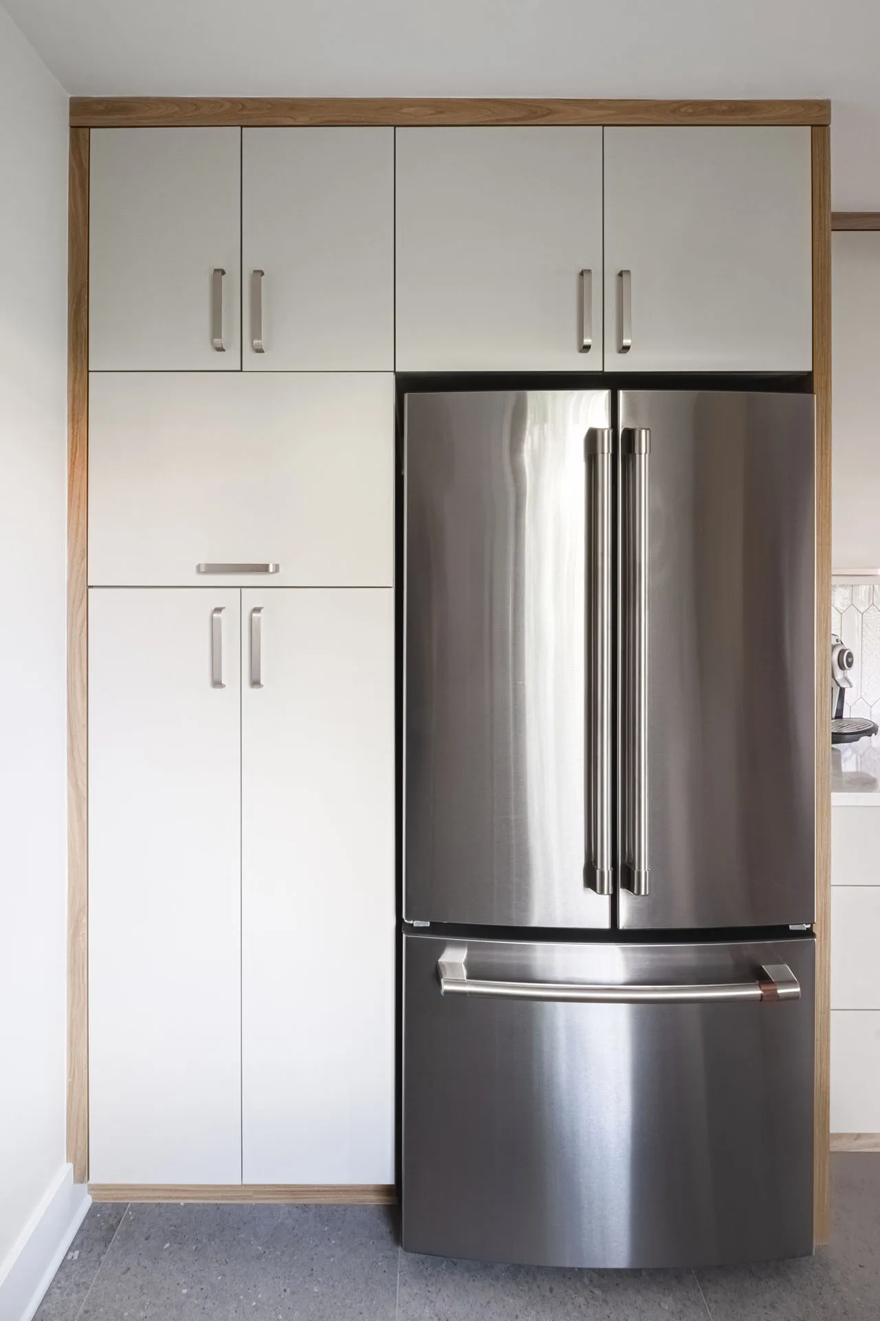 Modern kitchen with white cabinets and wood frame, stainless steel refrigerator, grey countertop
