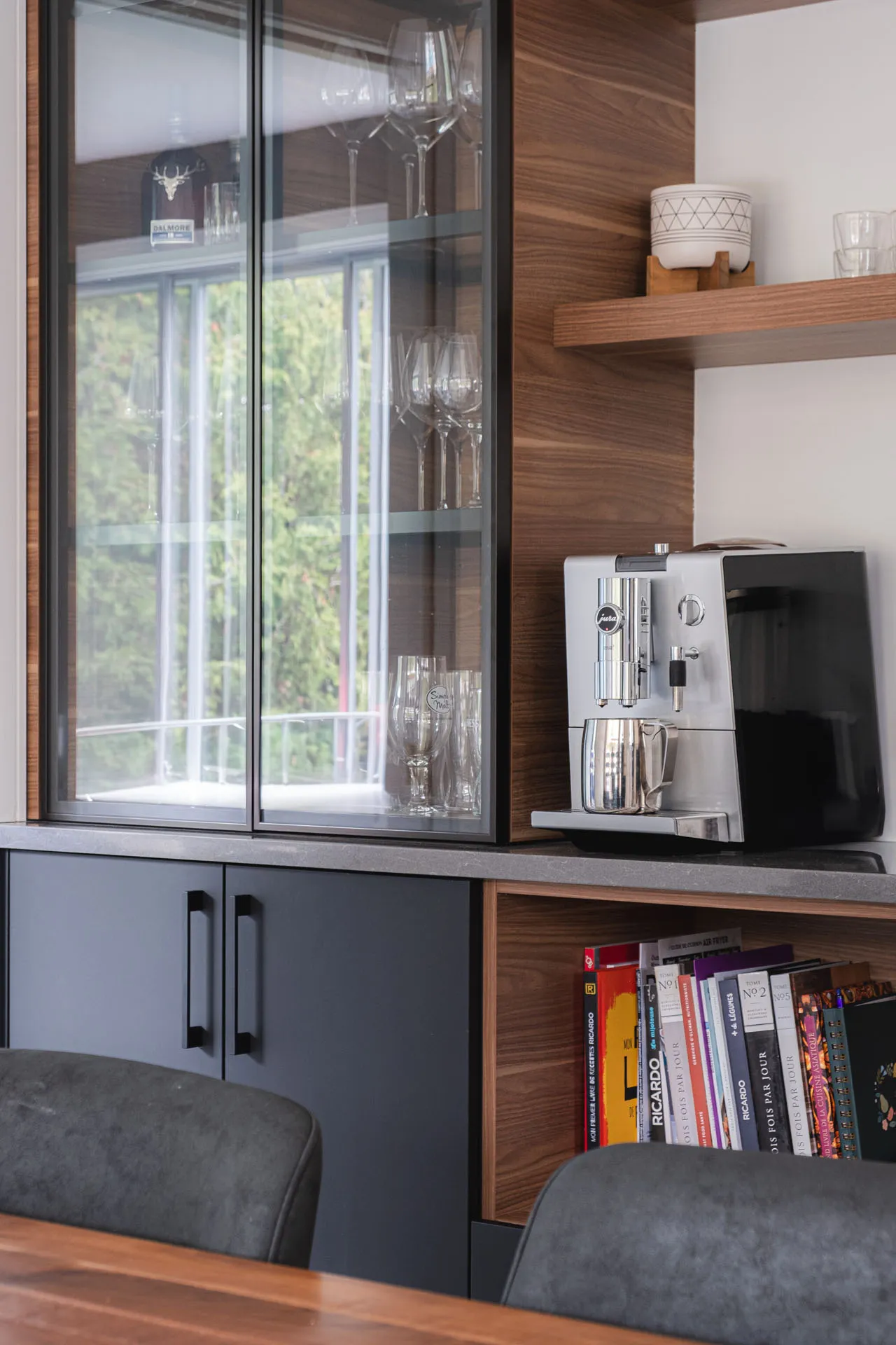 Kitchen cabinets walnut wood and charcoal gray with gray countertop, glass display cabinets and open shelving, built-in coffee maker.