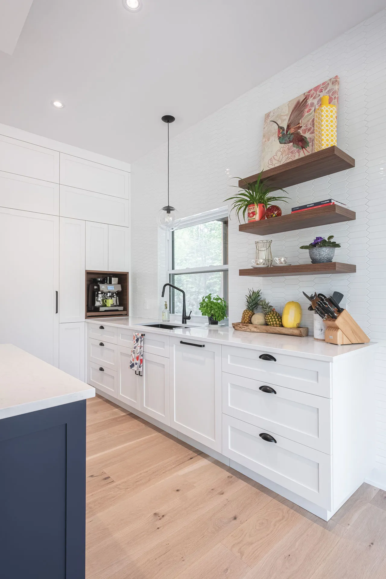 White kitchen with navy blue island, white countertop, Menuitech cabinetry, white subway tile backsplash, wooden shelves