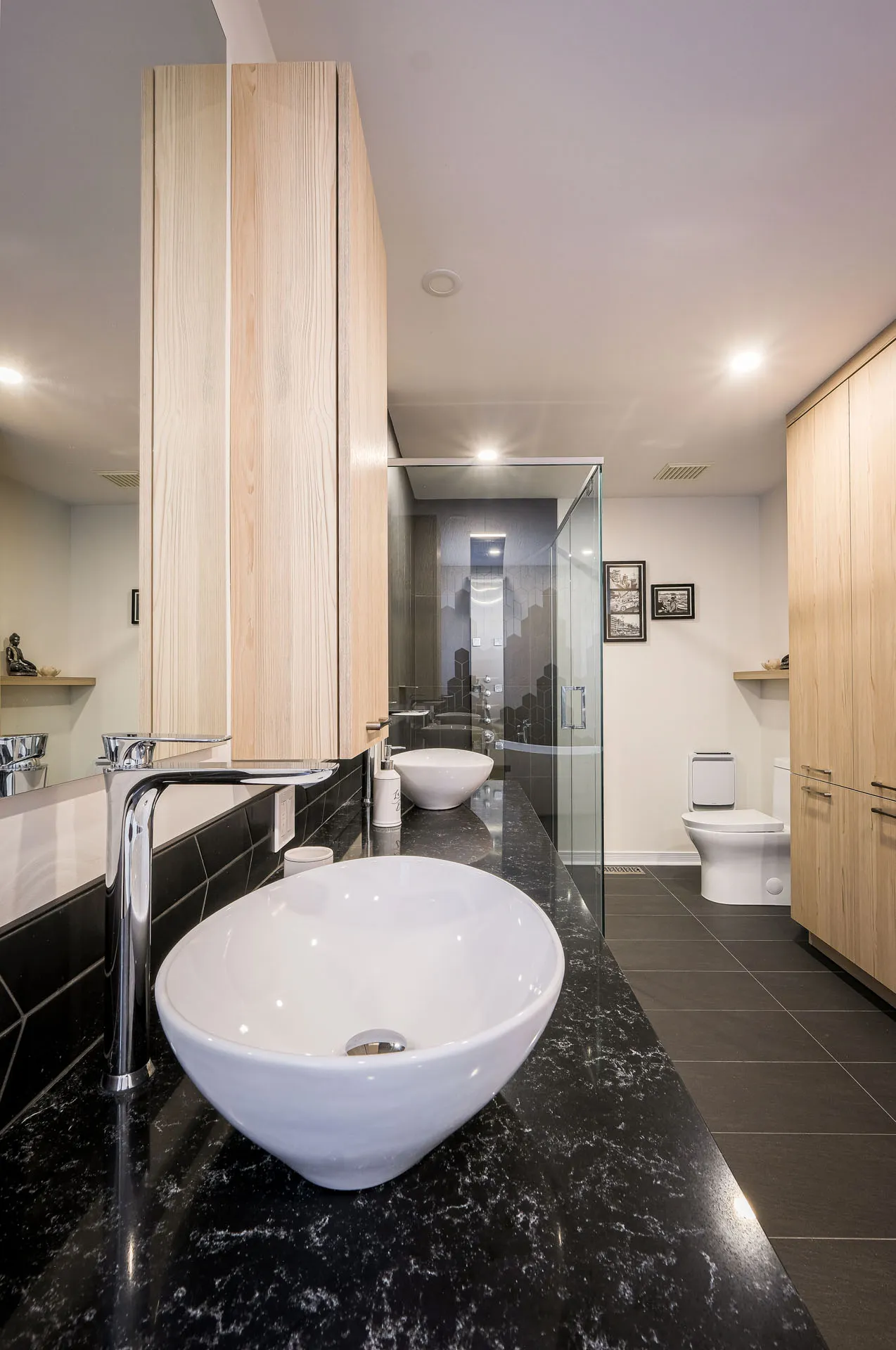 Modern Landry bathroom: light wood cabinets, black granite countertop, round white vessel sink, glass shower enclosure, wood mirror