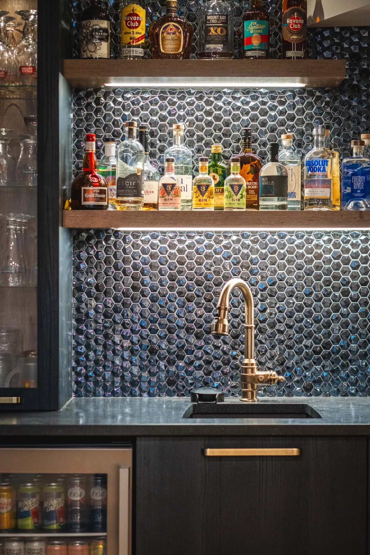 Bar noir avec dosseret hexagonal bleu, comptoir gris, étagères bois, robinet laiton et bouteilles alcool