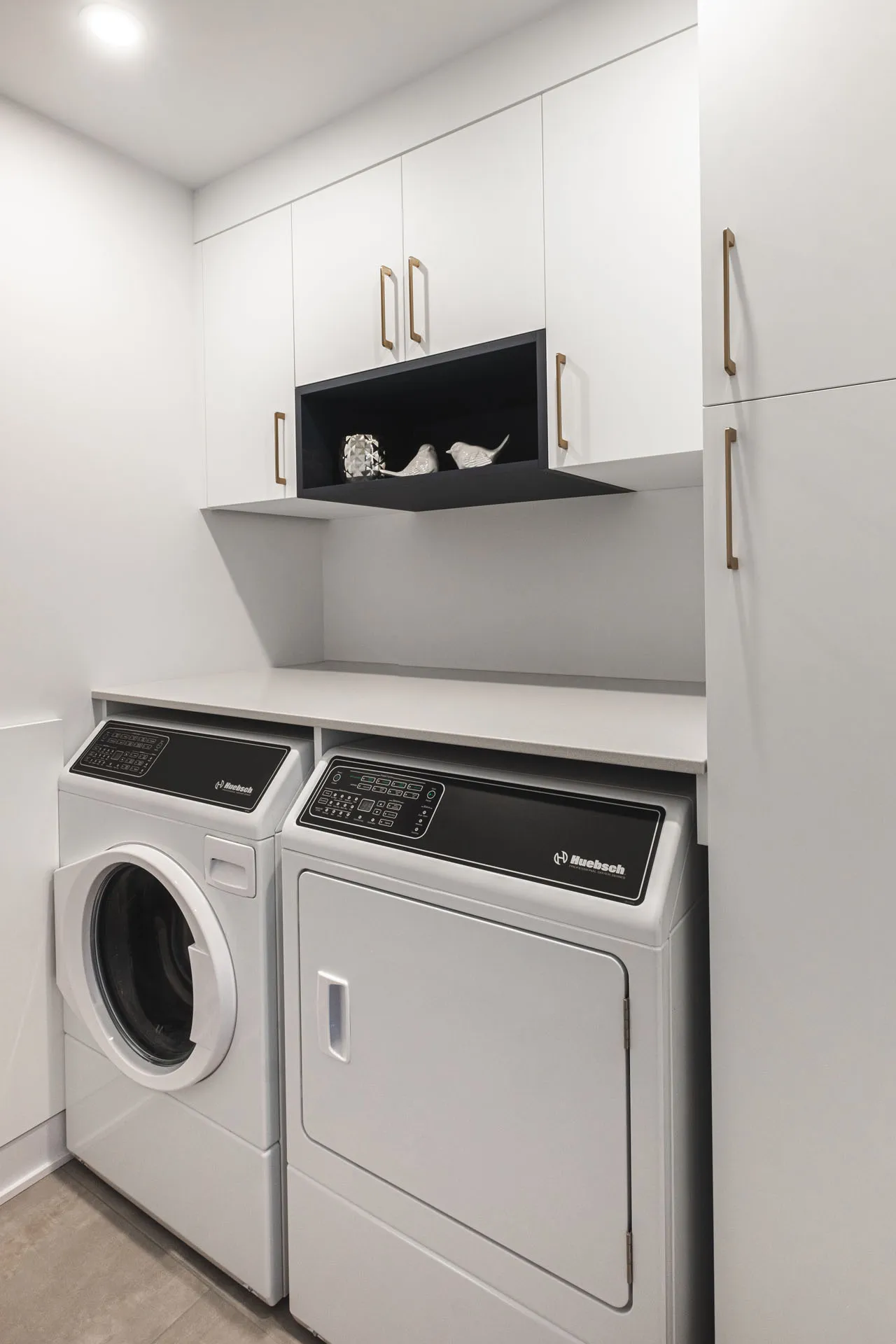 Modern laundry room with white Menuitech cabinets, grey countertop, black backsplash and white appliances