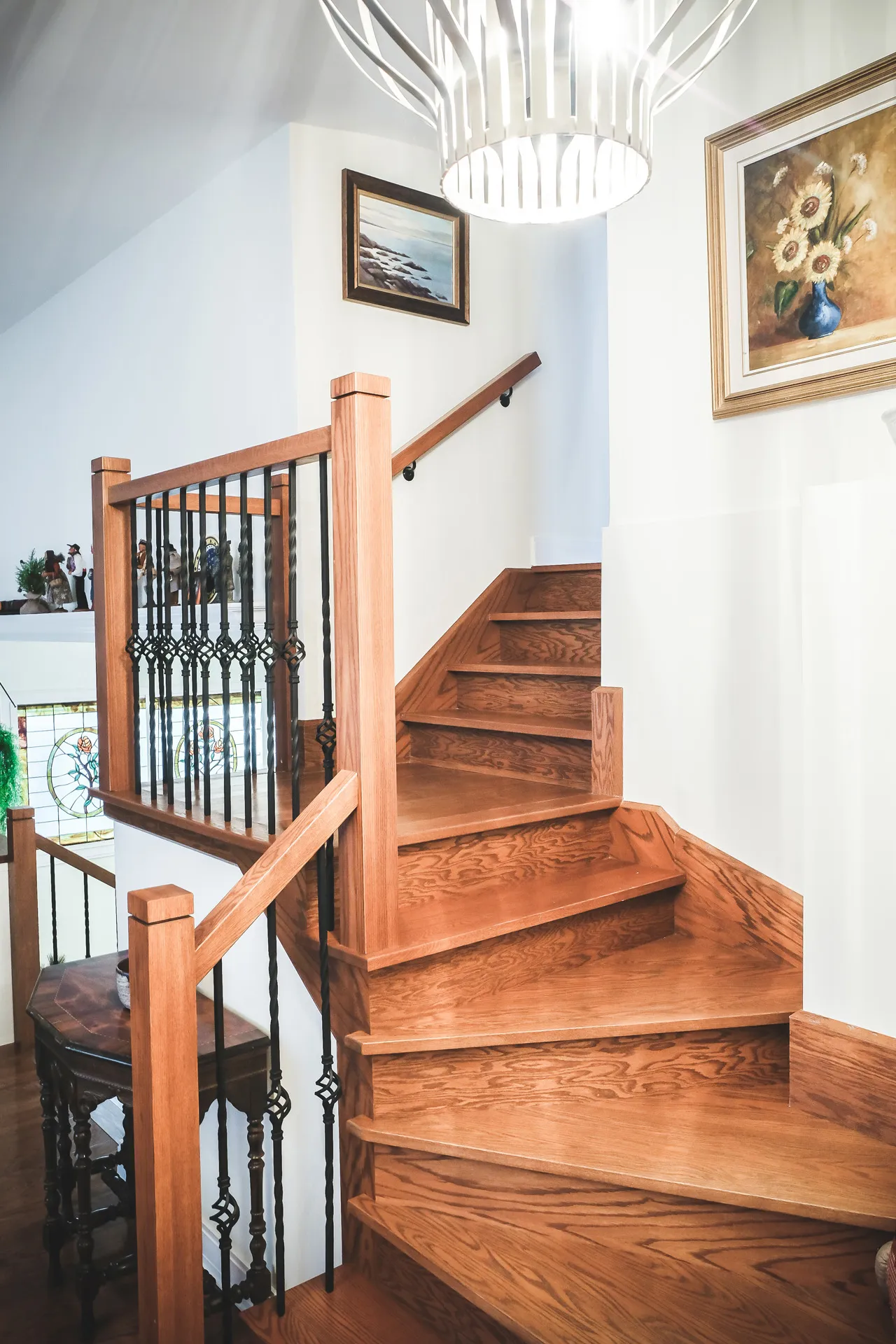 Hardwood staircase with black balusters and railing, modern pendant light, white walls and framed artwork