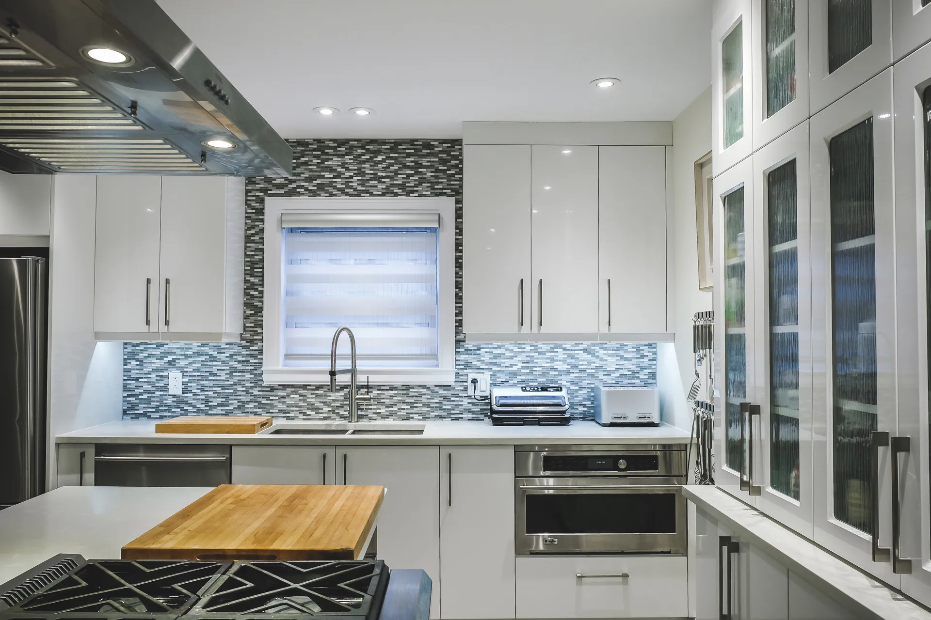Menuitech Phaneuf kitchen: white cabinets, blue-grey tile backsplash, white countertop, wooden island, stainless steel appliances.