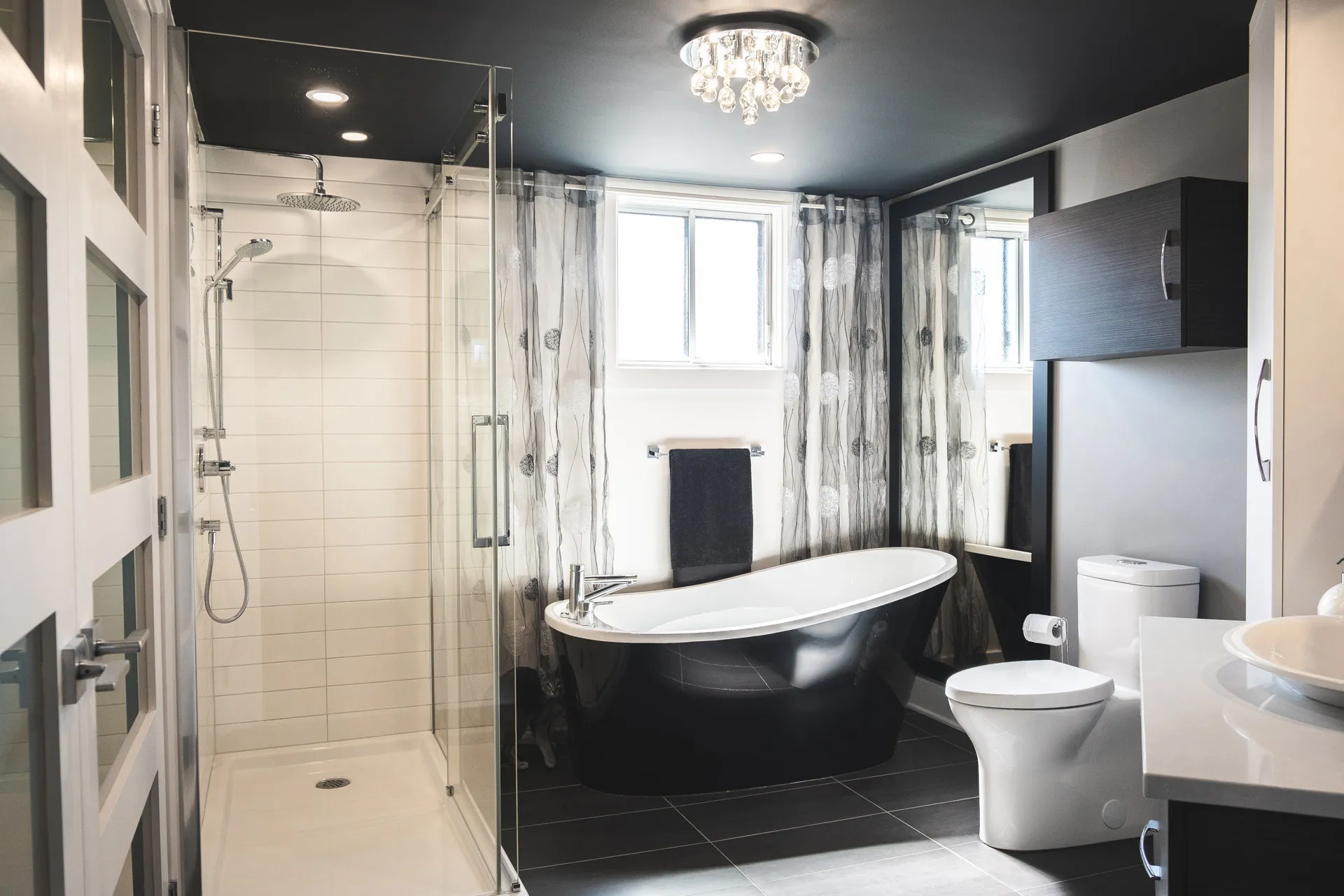 Modern Menuitech bathroom with black soaking tub, glass shower enclosure, grey cabinetry and white countertop