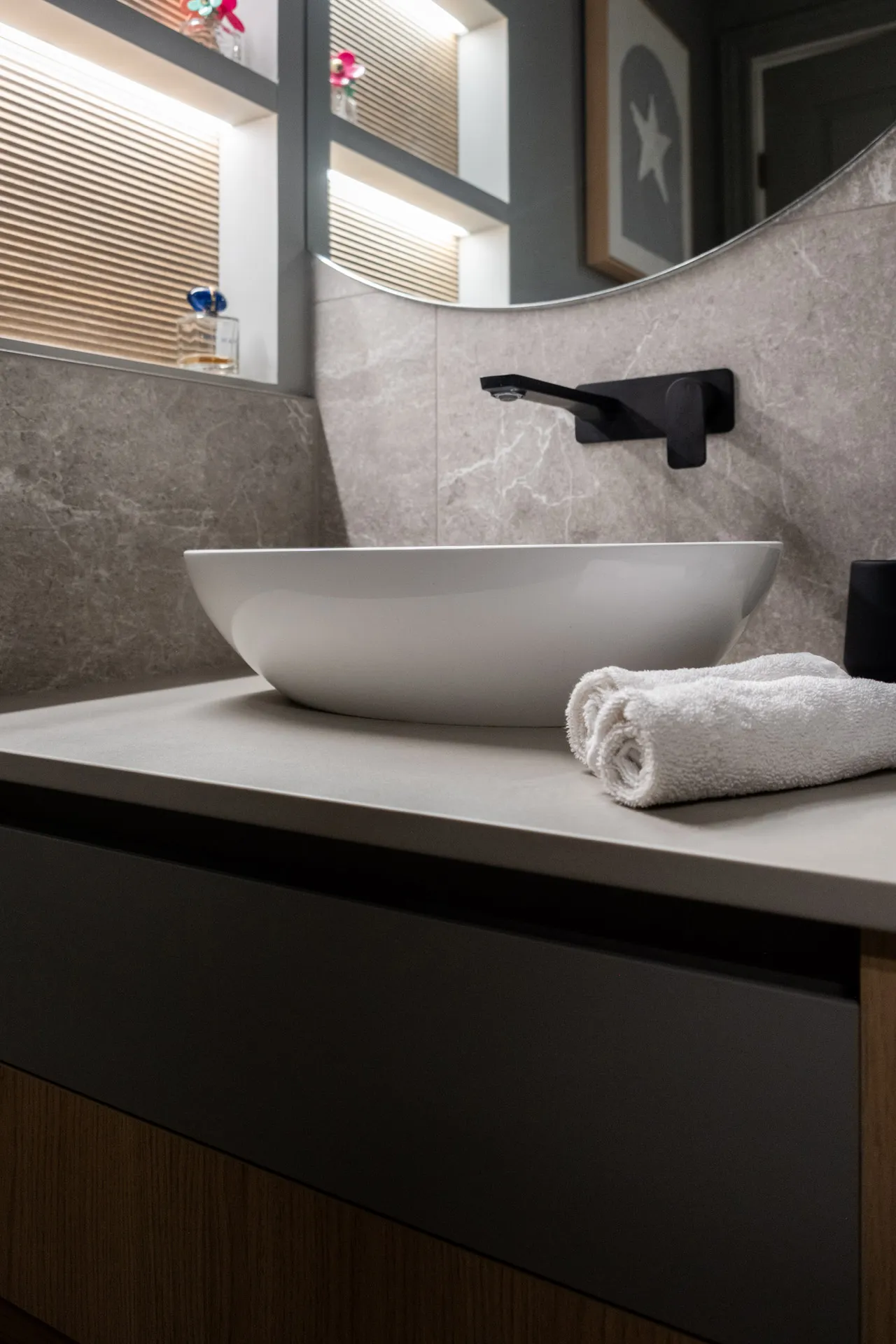 Salle de bain Garraud : vanité noire avec comptoir blanc, lavabo ovale blanc, robinet mural noir, miroir éclairé et dosseret gris.