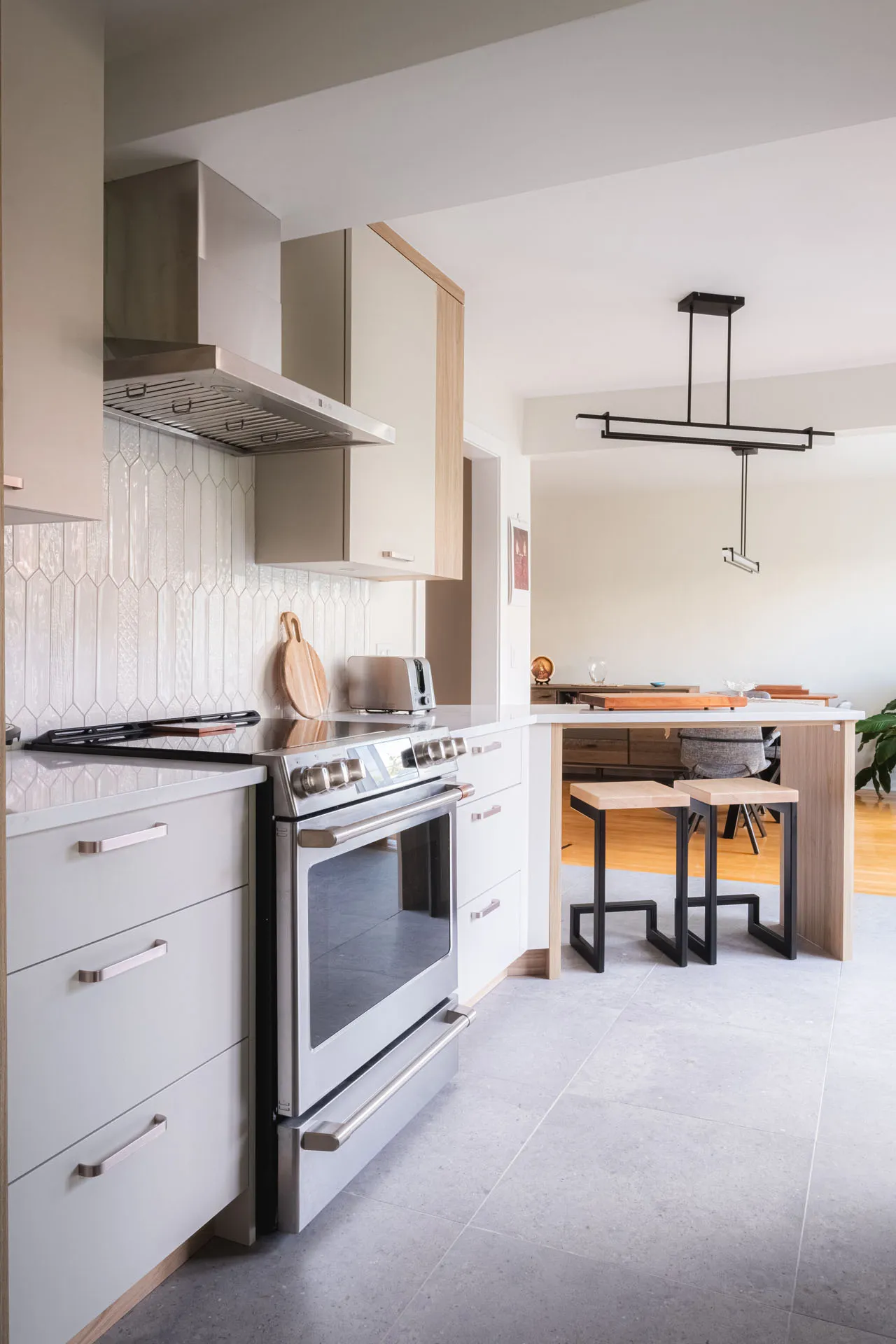 Modern white kitchen with custom cabinetry, grey countertop, wooden island, geometric white backsplash and black pendant lighting