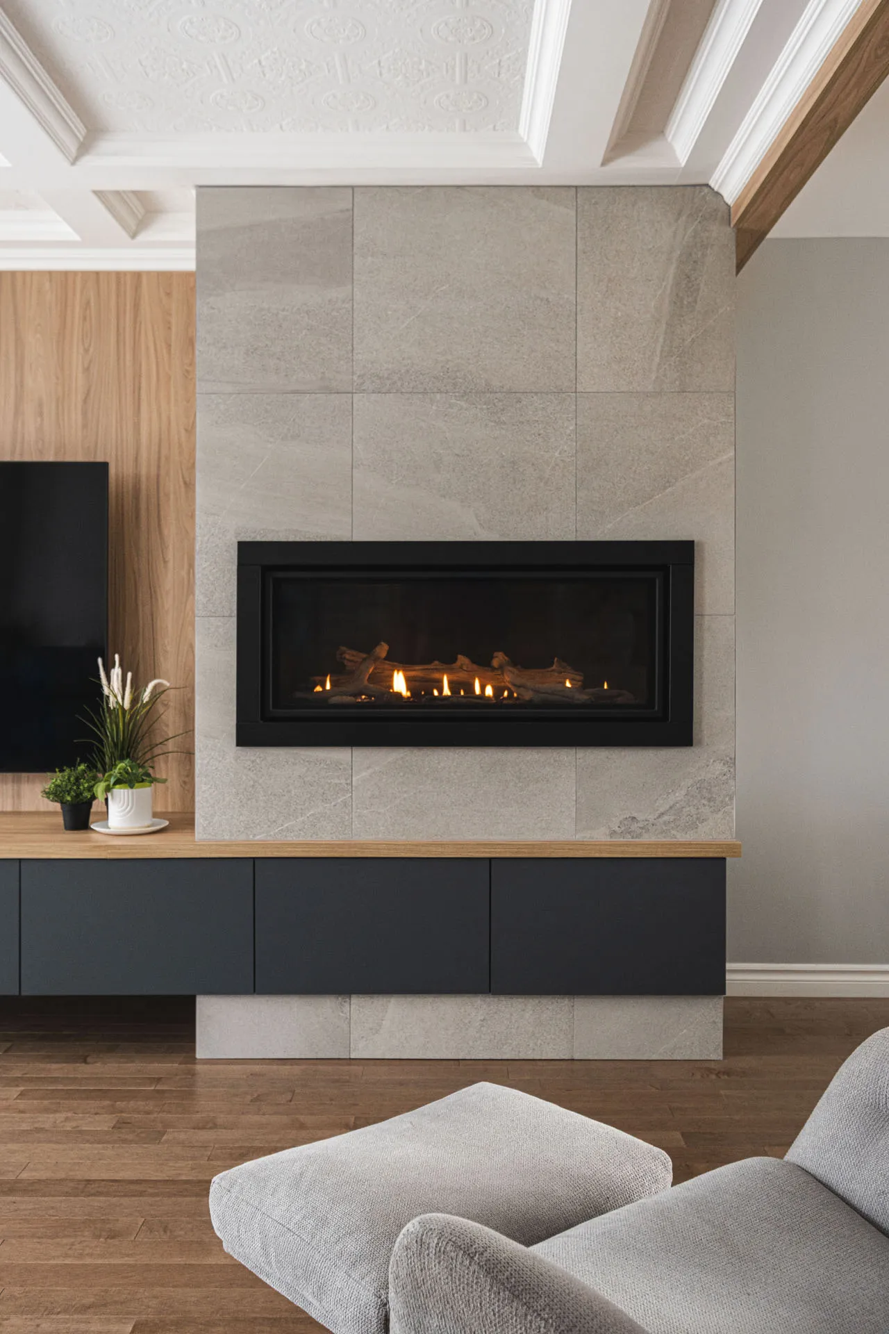 Modern living room with linear built-in fireplace, grey stone wall, black TV unit and natural wood countertop