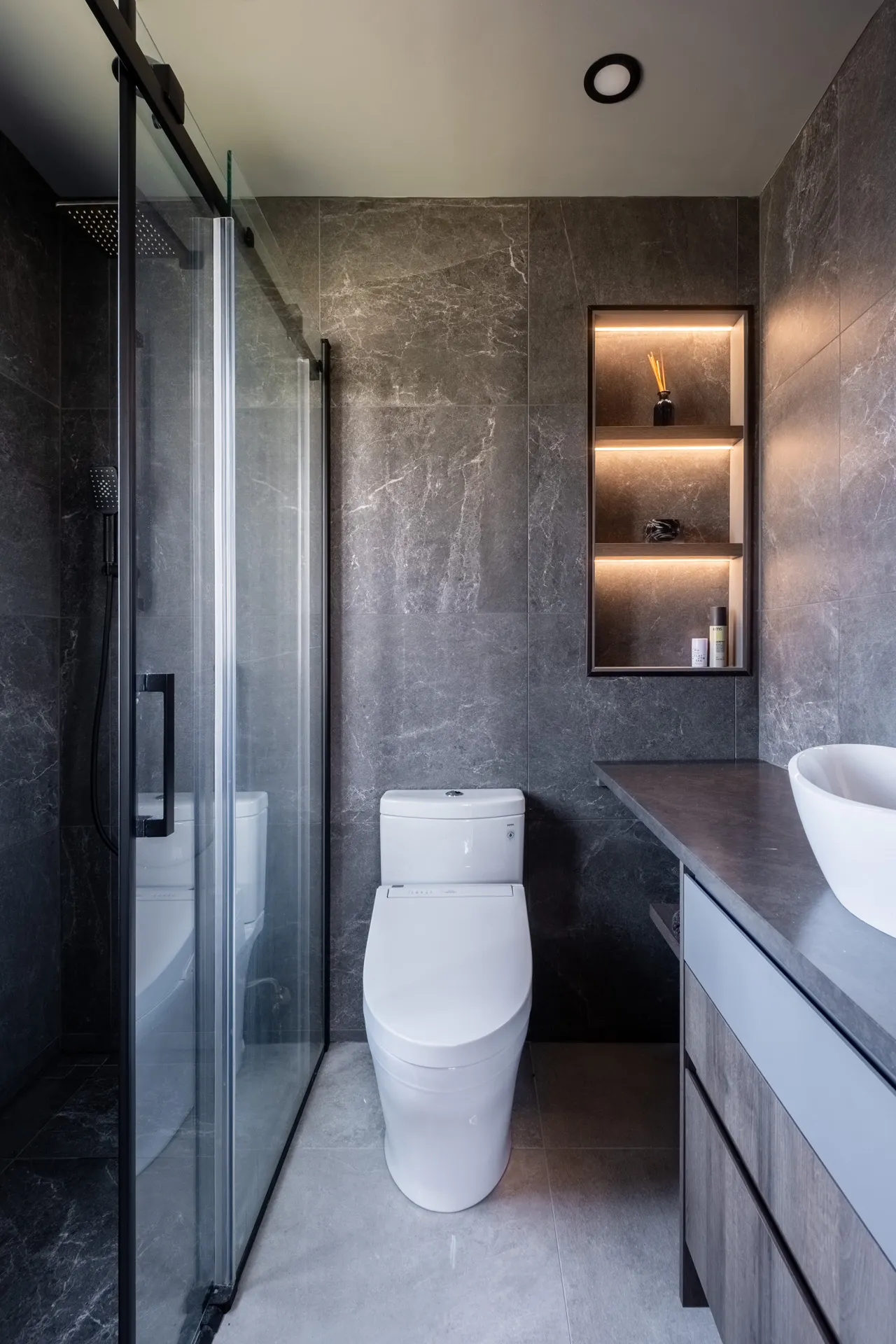 Salle de bain moderne Garraud Rosemère : armoires grises, comptoir anthracite, niche murale éclairée, toilette blanche, douche vitrée