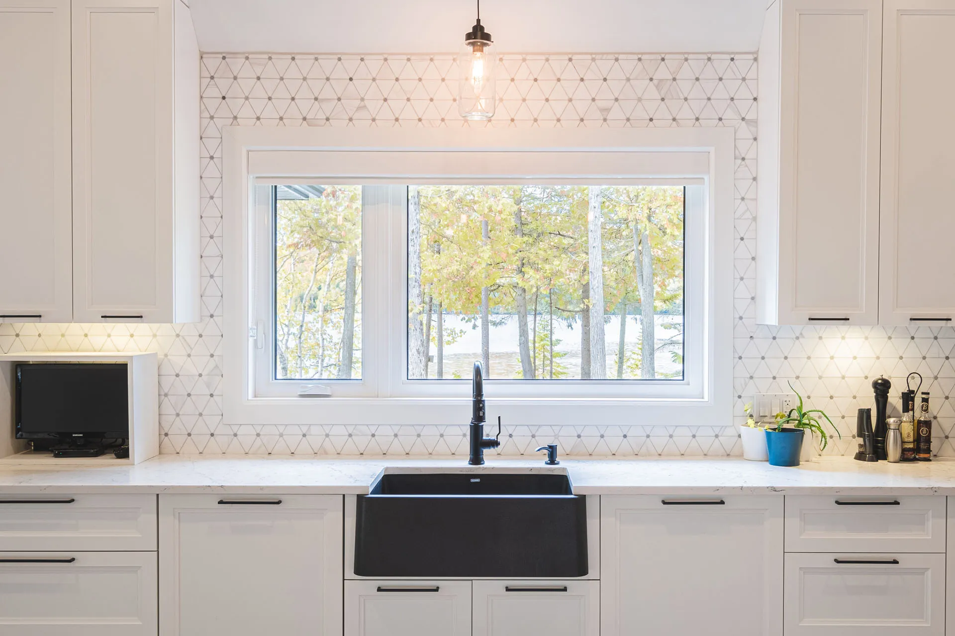Modern white kitchen with Menuitech cabinets, white countertop, gray geometric backsplash, black sink and panoramic window