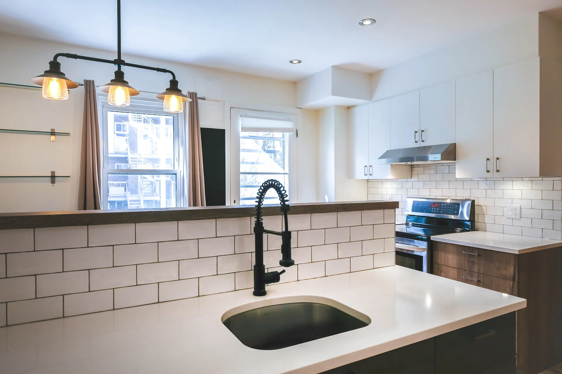 Modern kitchen with white cabinets, dark wood island, white countertops, white subway tile backsplash and black pendant lights.