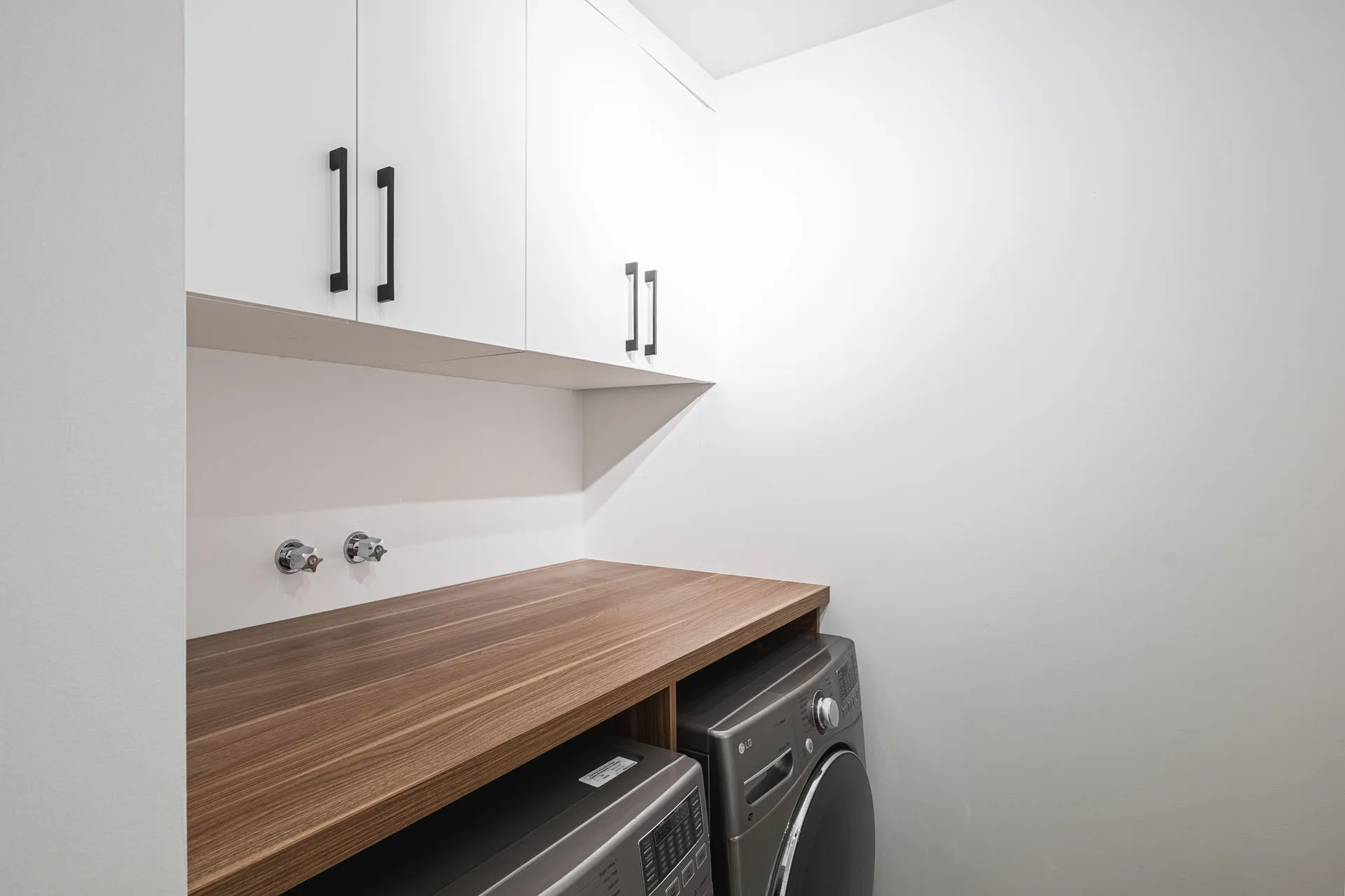 Modern bathroom with white cabinets, wooden countertop, grey washer and integrated sink