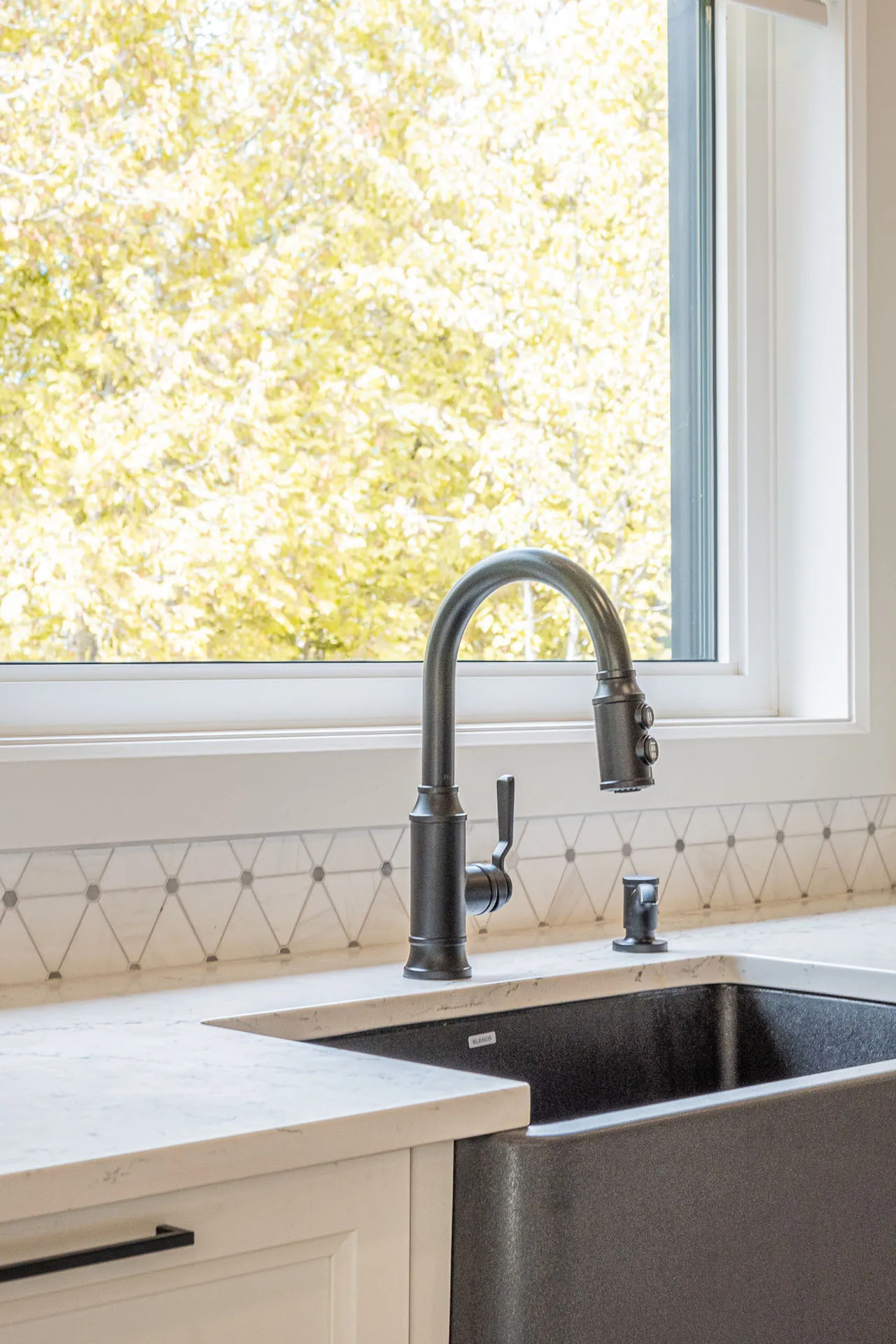 Simard kitchen: light quartz countertop, light wood cabinets, black faucet, geometric tile backsplash