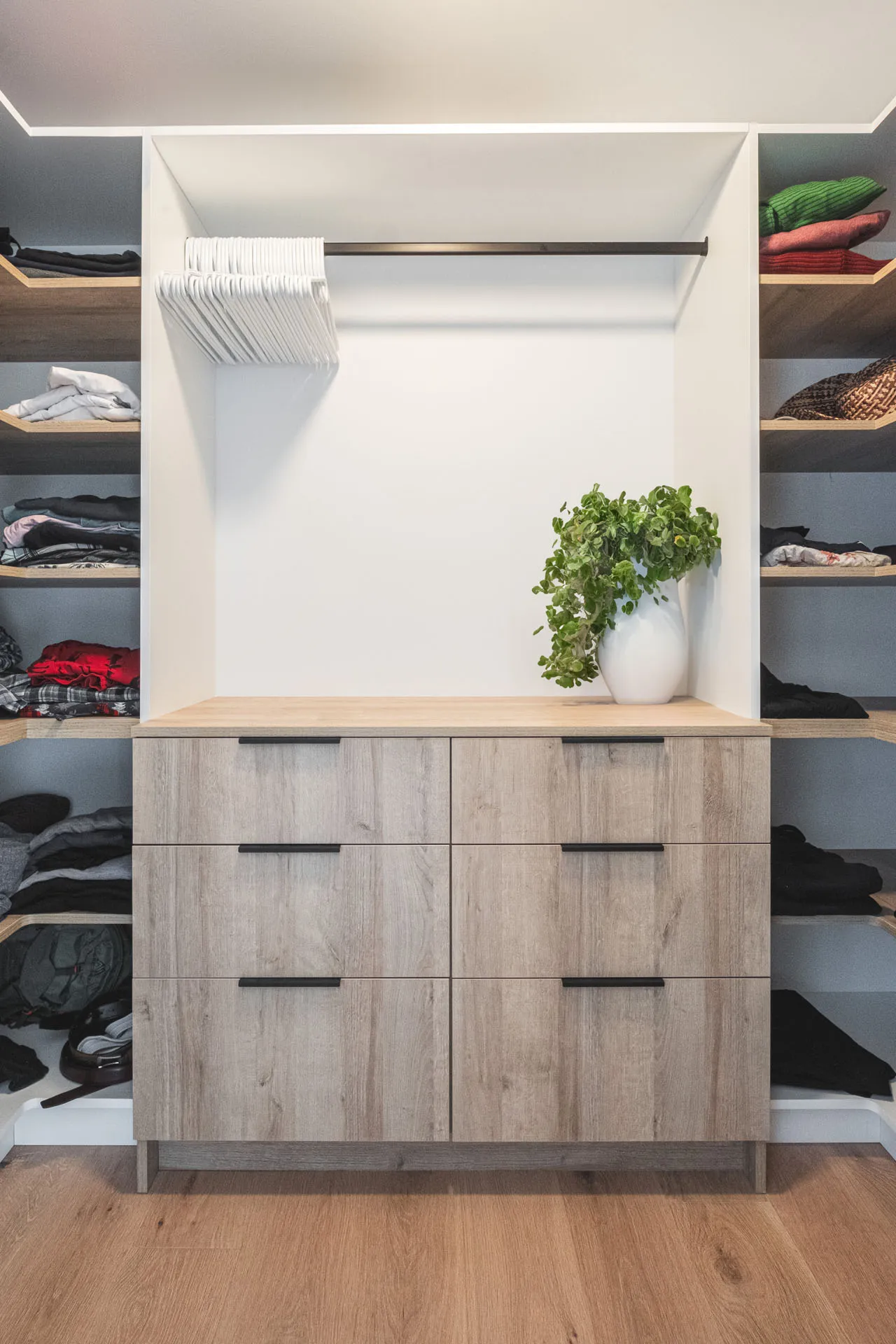 Walk-in closet with white and light wood cabinets, 6-drawer storage island, grey shelves, wood countertop, green plant