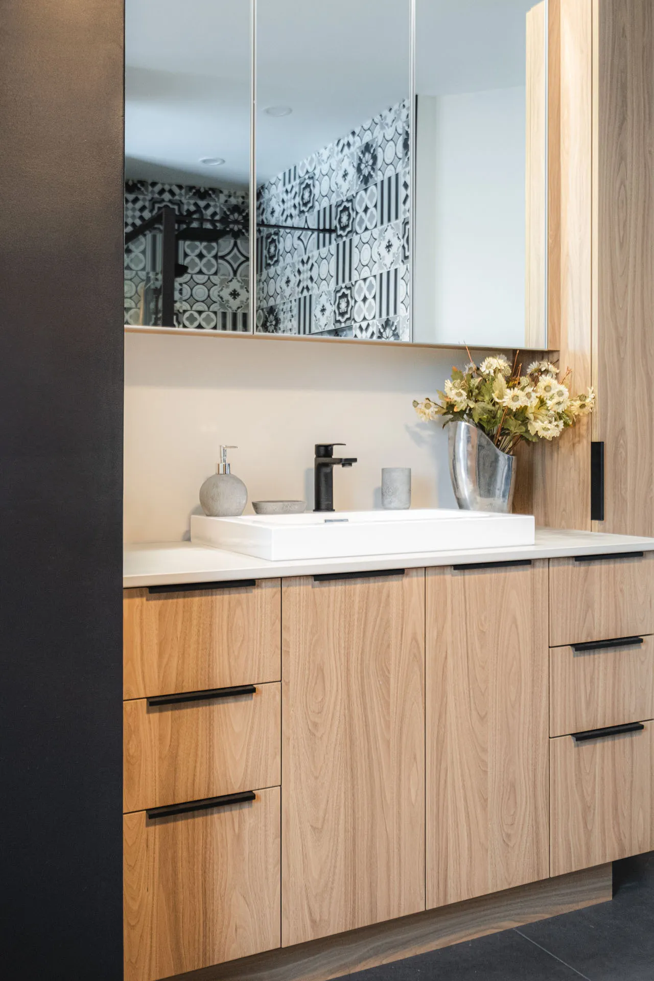 Modern bathroom with light wood vanity, white countertop, mirrored cabinet and geometric tile backsplash
