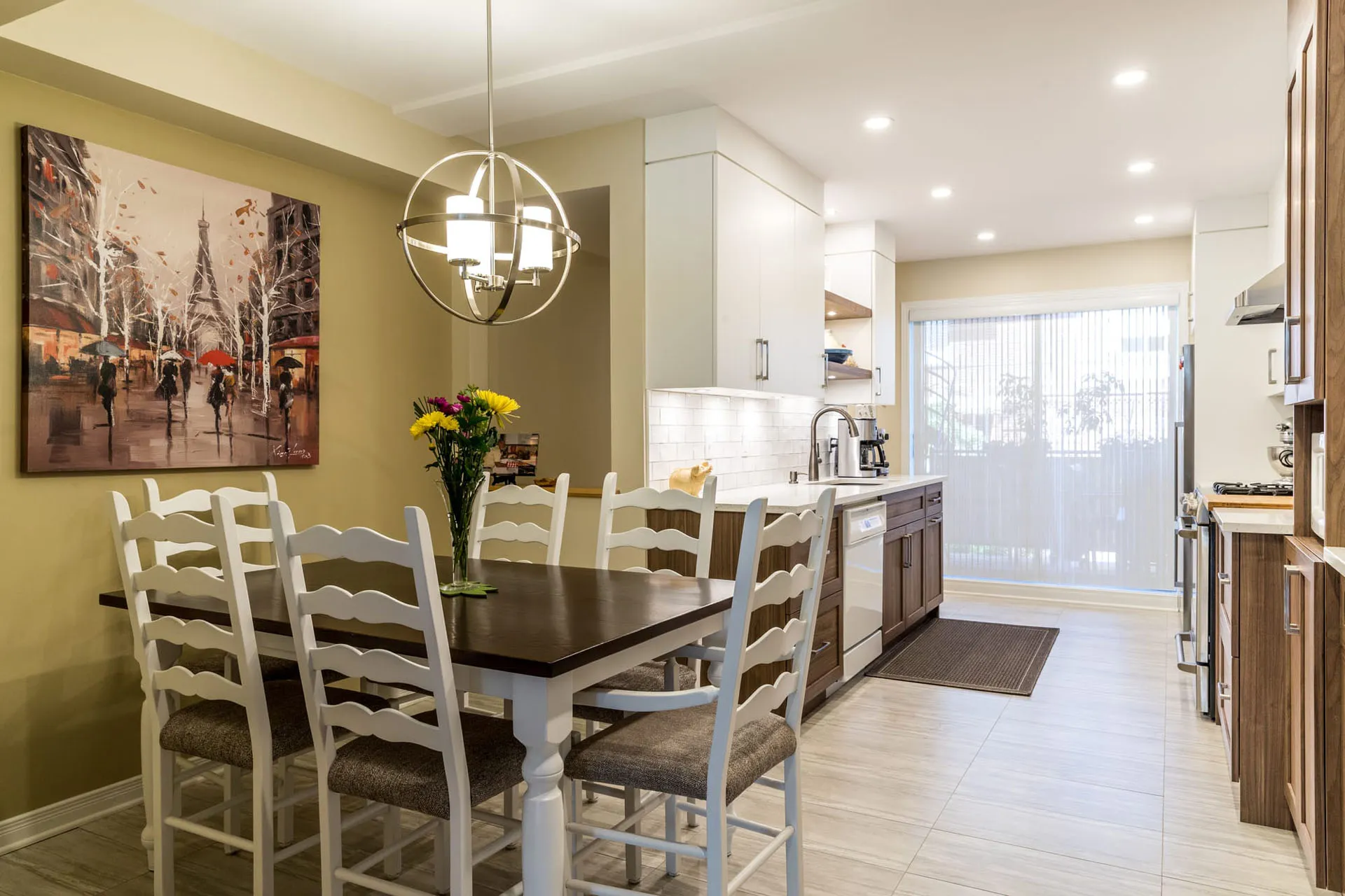 Open kitchen with white cabinetry, black countertop, center island, white subway backsplash and spherical pendant light fixture.