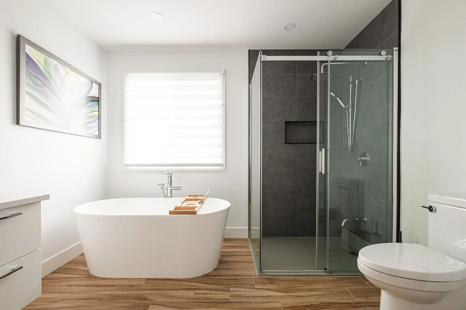 Modern bathroom with white freestanding soaking tub, glass shower enclosure, white cabinetry, wood countertop, grey tile and toilet
