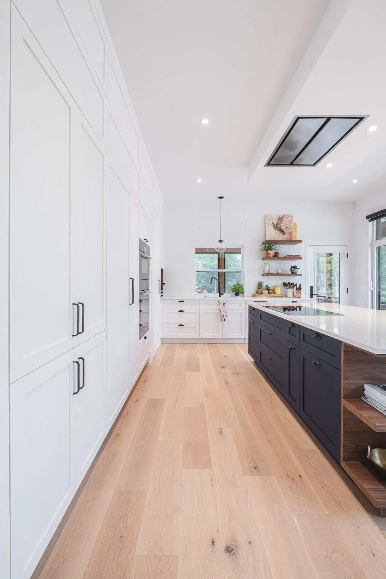 Modern Menuitech kitchen with white cabinetry and black island, white countertops, light wood flooring, white tile backsplash