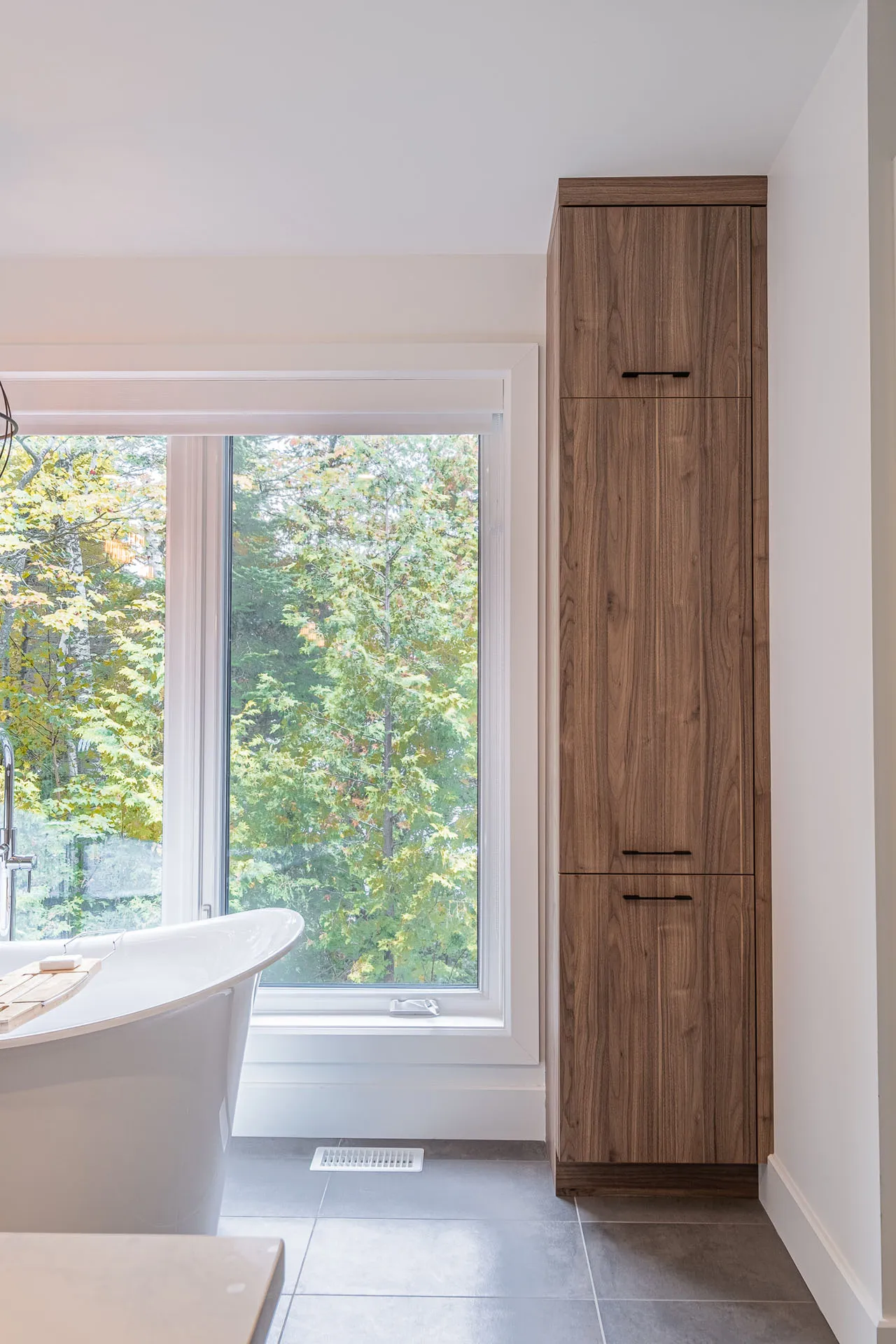 Modern bathroom with walnut wood wall cabinet, white soaking tub and panoramic forest view window