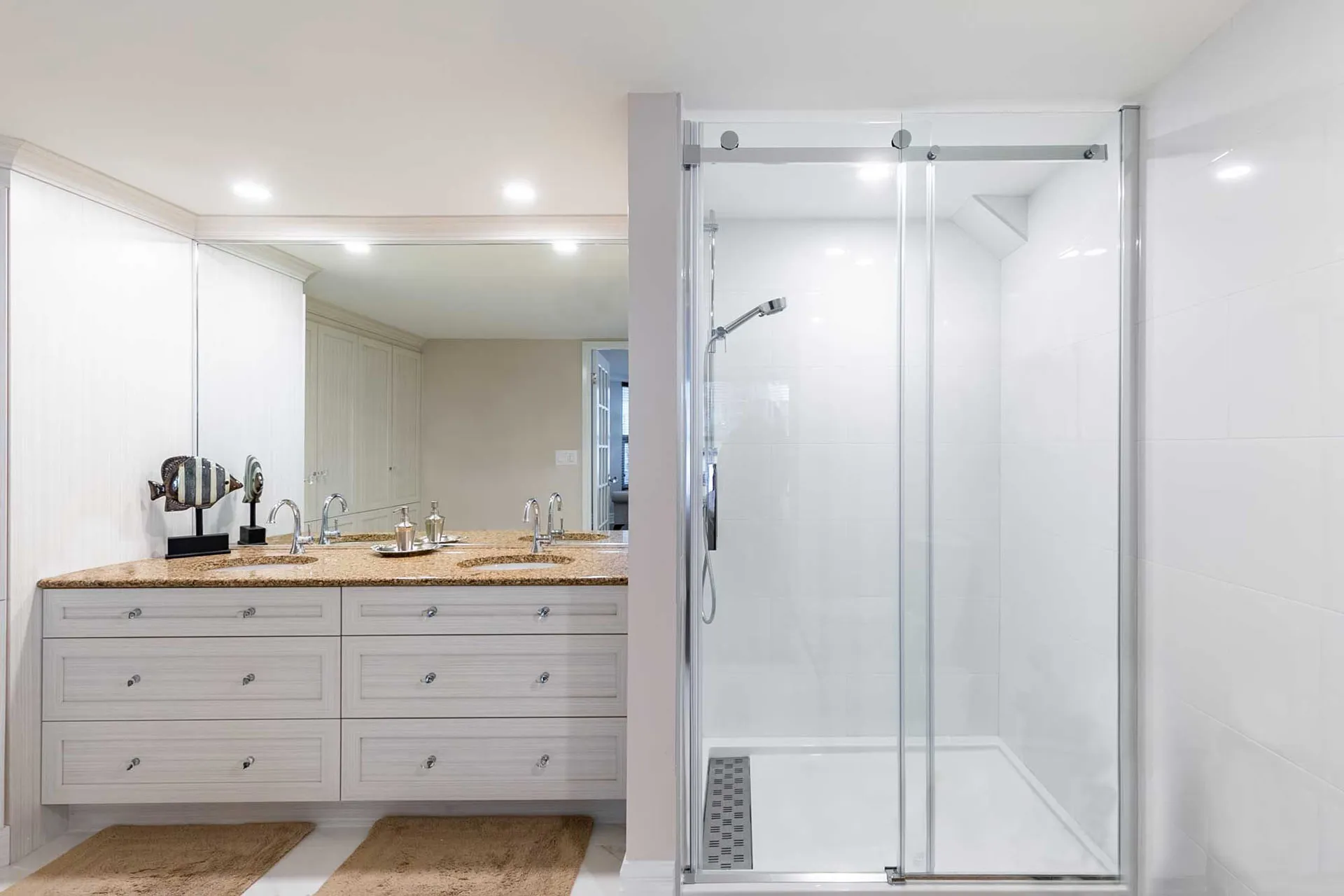Modern bathroom with white cabinetry, beige granite countertop, double sink and glass shower enclosure in Repentigny