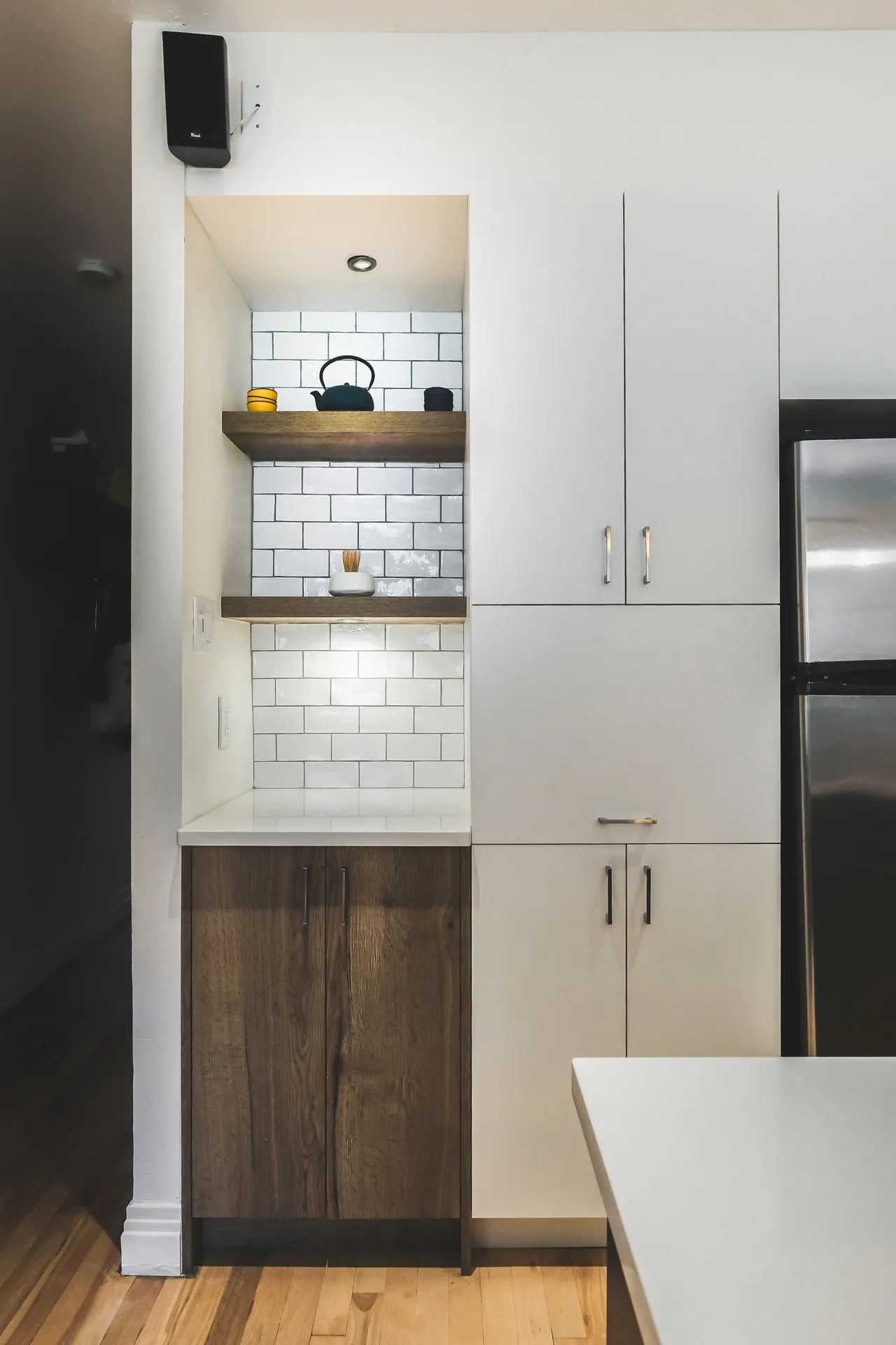 Modern kitchen with white and dark wood cabinets, white countertop, white subway tile backsplash, floating shelves and stainless steel appliances