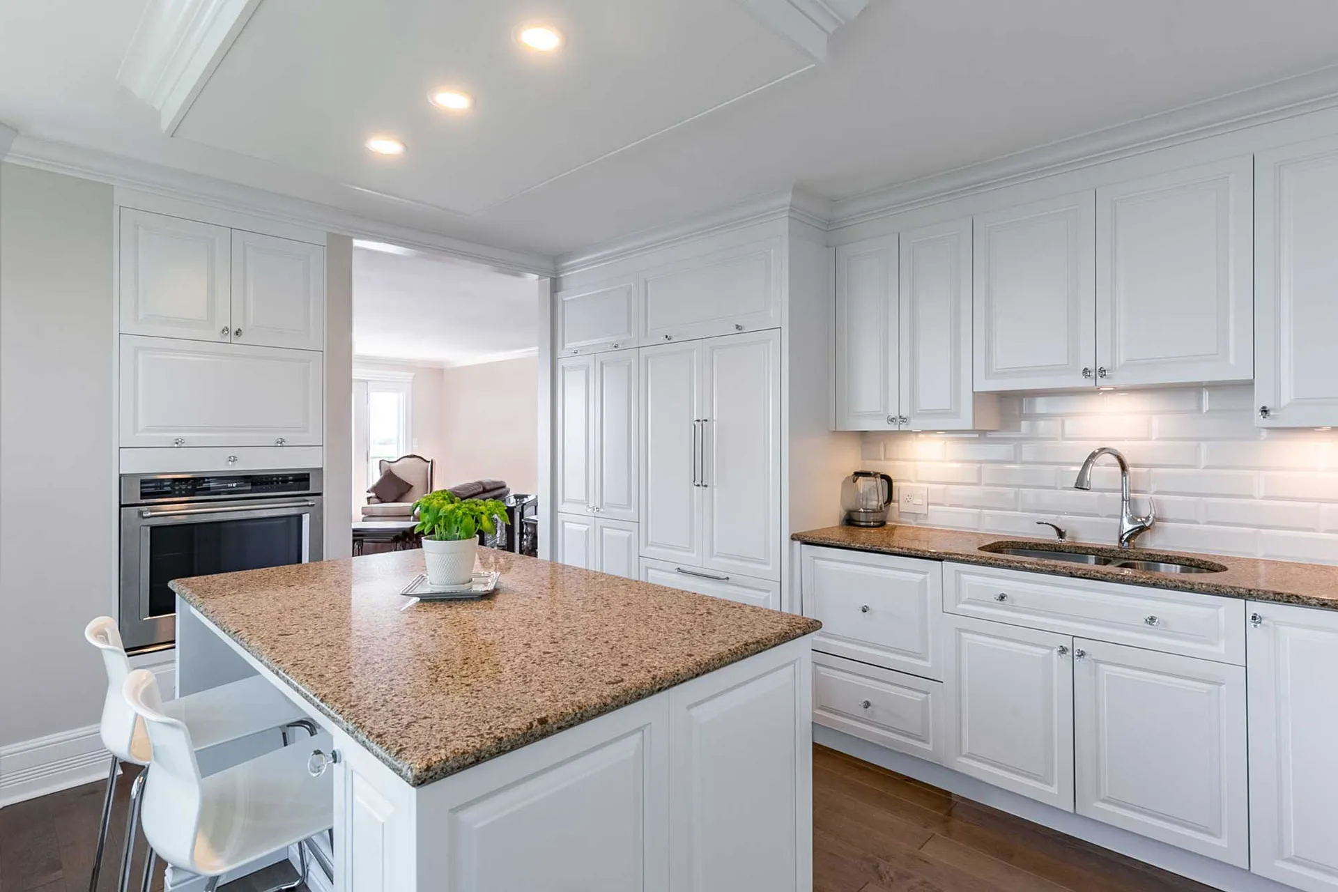 Modern white kitchen with island, brown granite countertop, white subway backsplash, Menuitech cabinets, recessed lighting