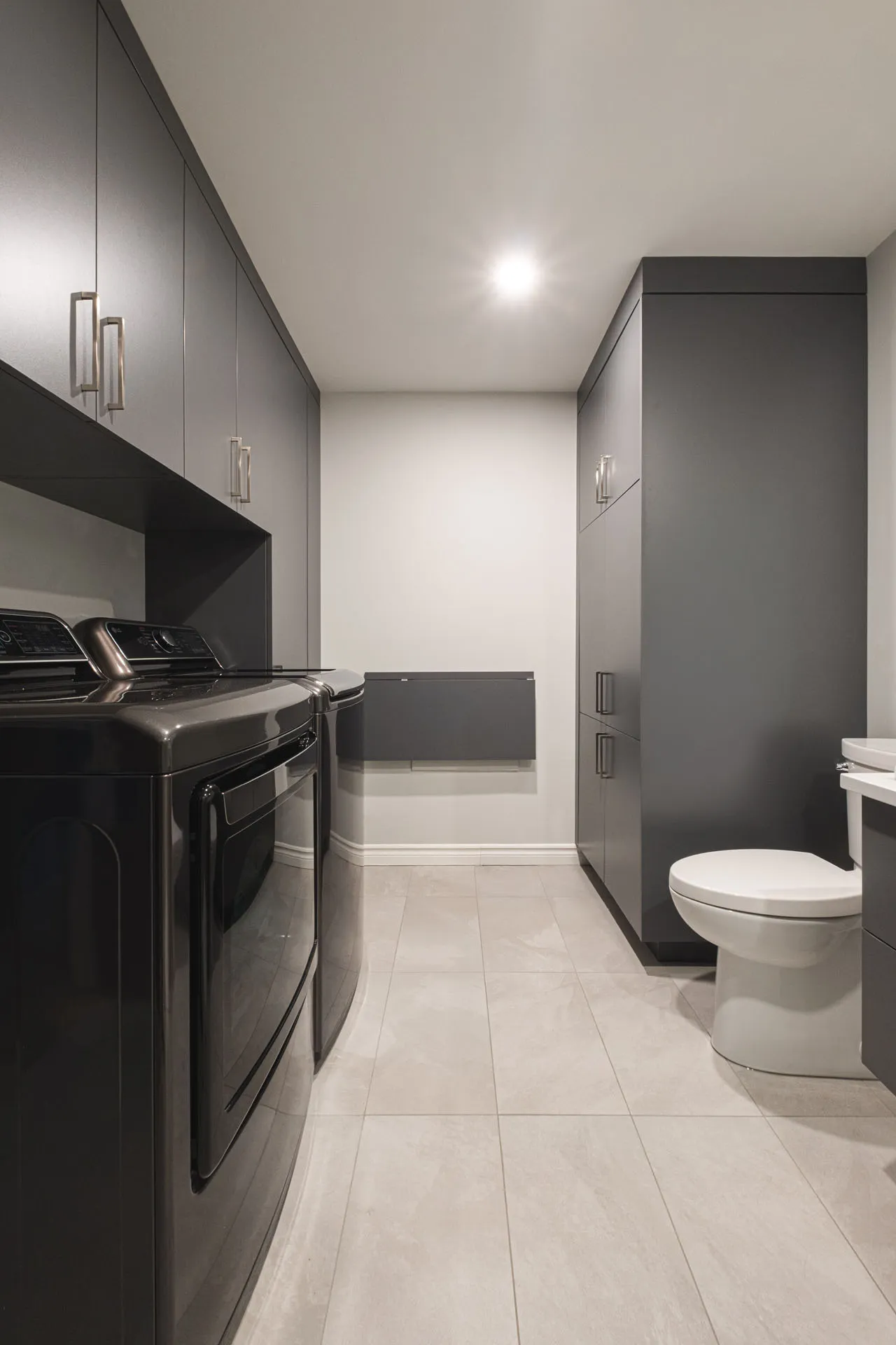 Modern bathroom with gray cabinets, gray quartz countertop, white toilet and black appliances