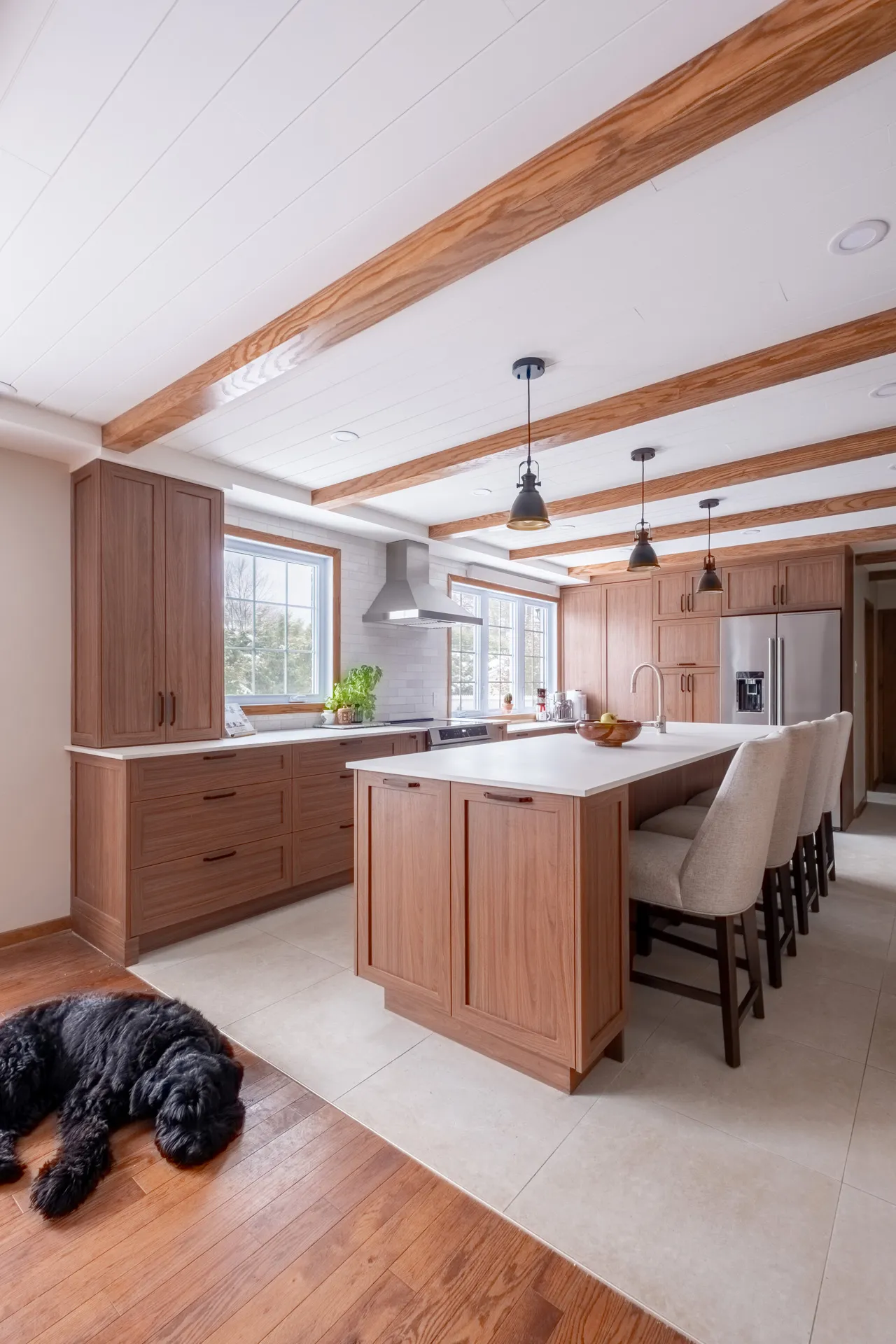 Lemay kitchen Laval: light walnut cabinets, white island countertop, wood beams, black pendant lights, tile backsplash.