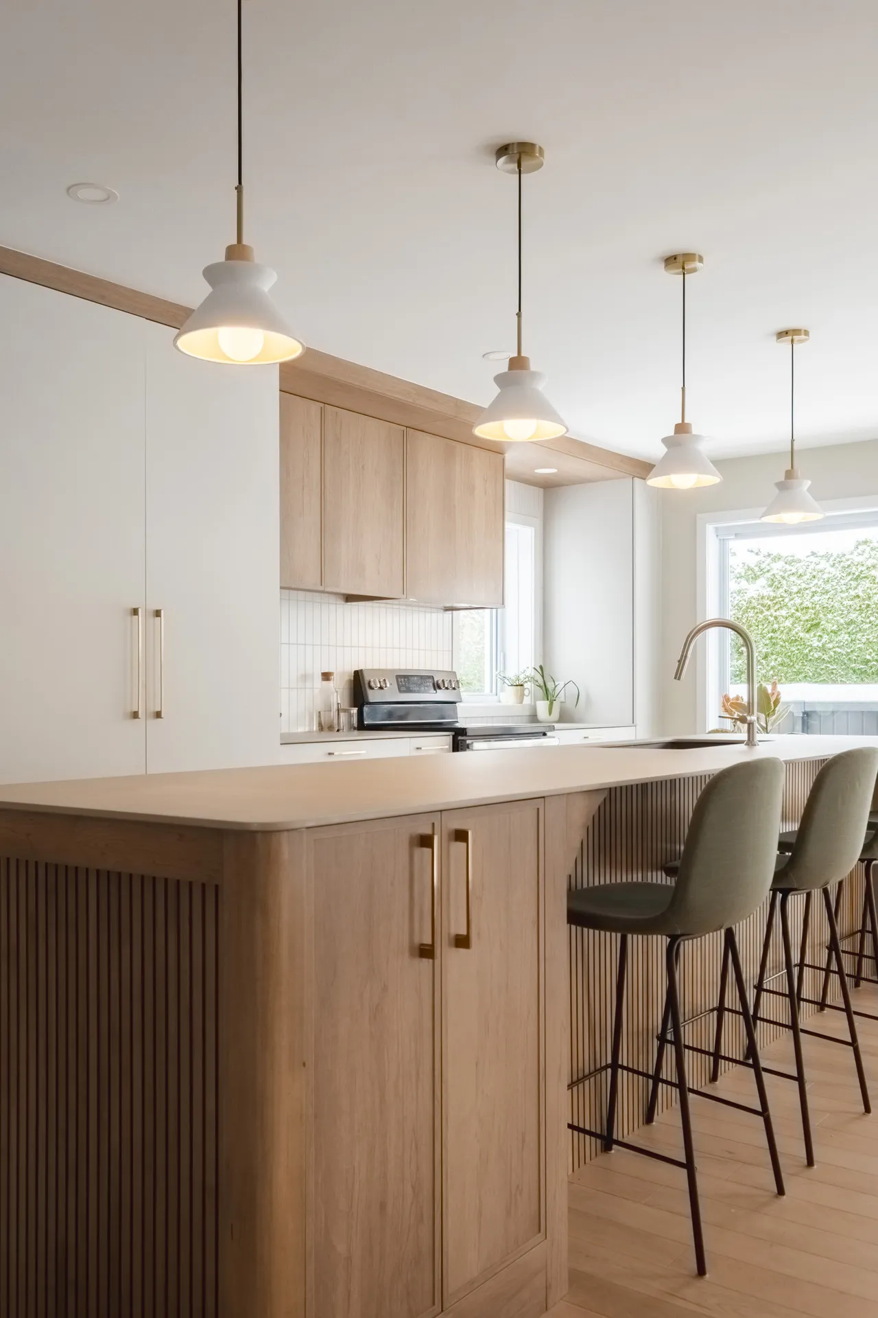 Cuisine moderne Léveillé avec armoires chêne clair, îlot bois, comptoir gris, dosseret carrelage blanc, luminaires suspendus laiton