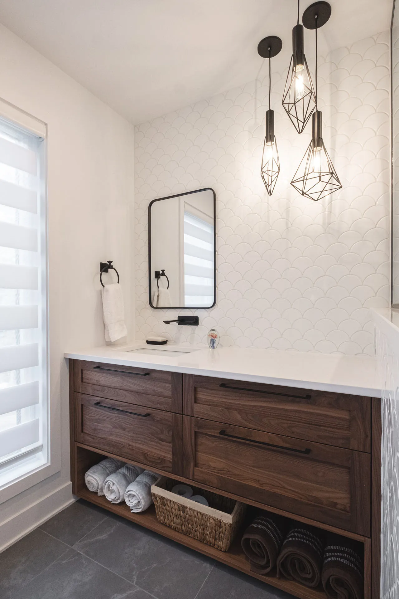 Menuitech bathroom with dark wood vanity, white countertop, white tile backsplash and black pendant lighting fixtures