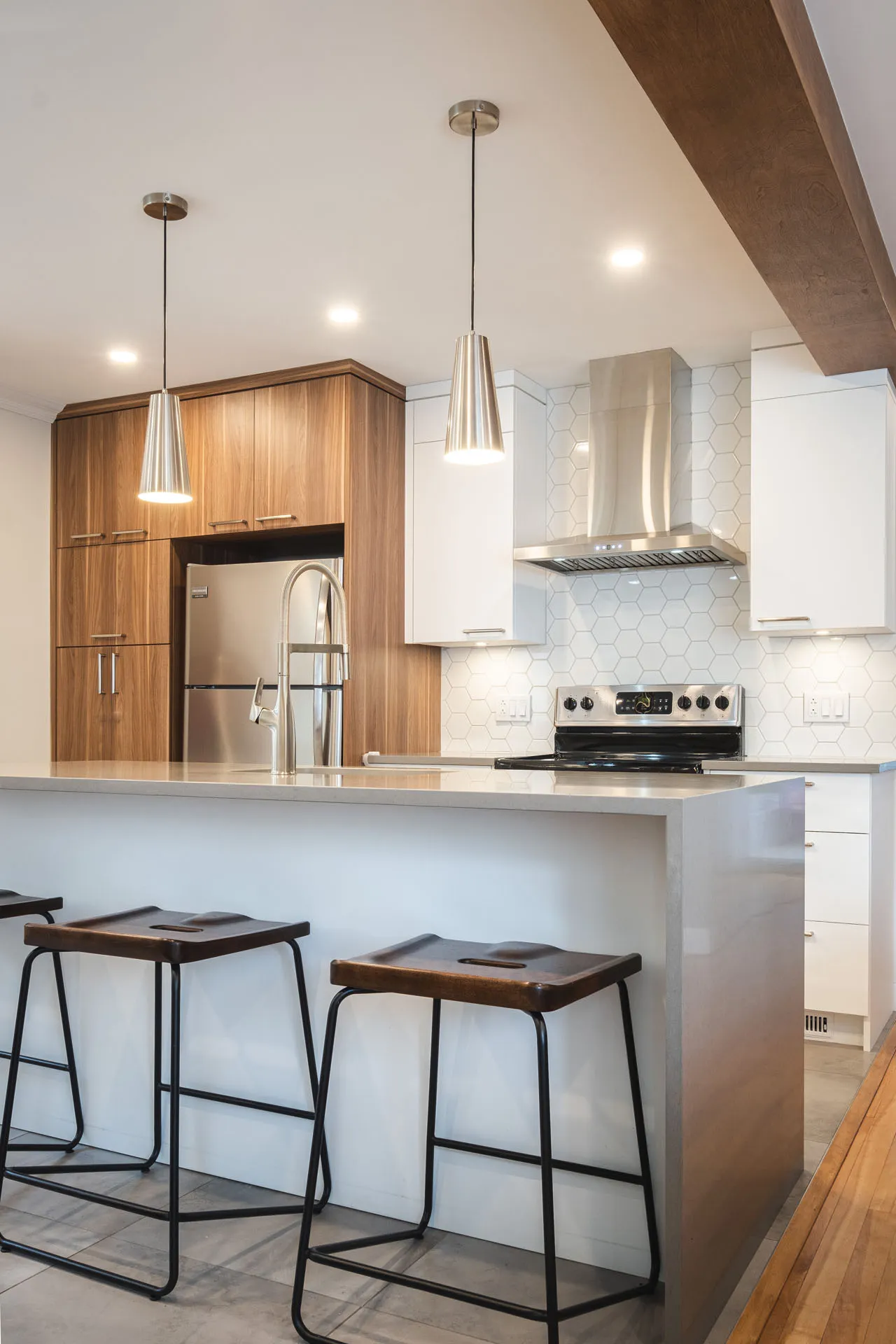 Modern Tardif kitchen with natural wood cabinets, white countertop, grey island, white hexagonal backsplash and chrome pendant lights
